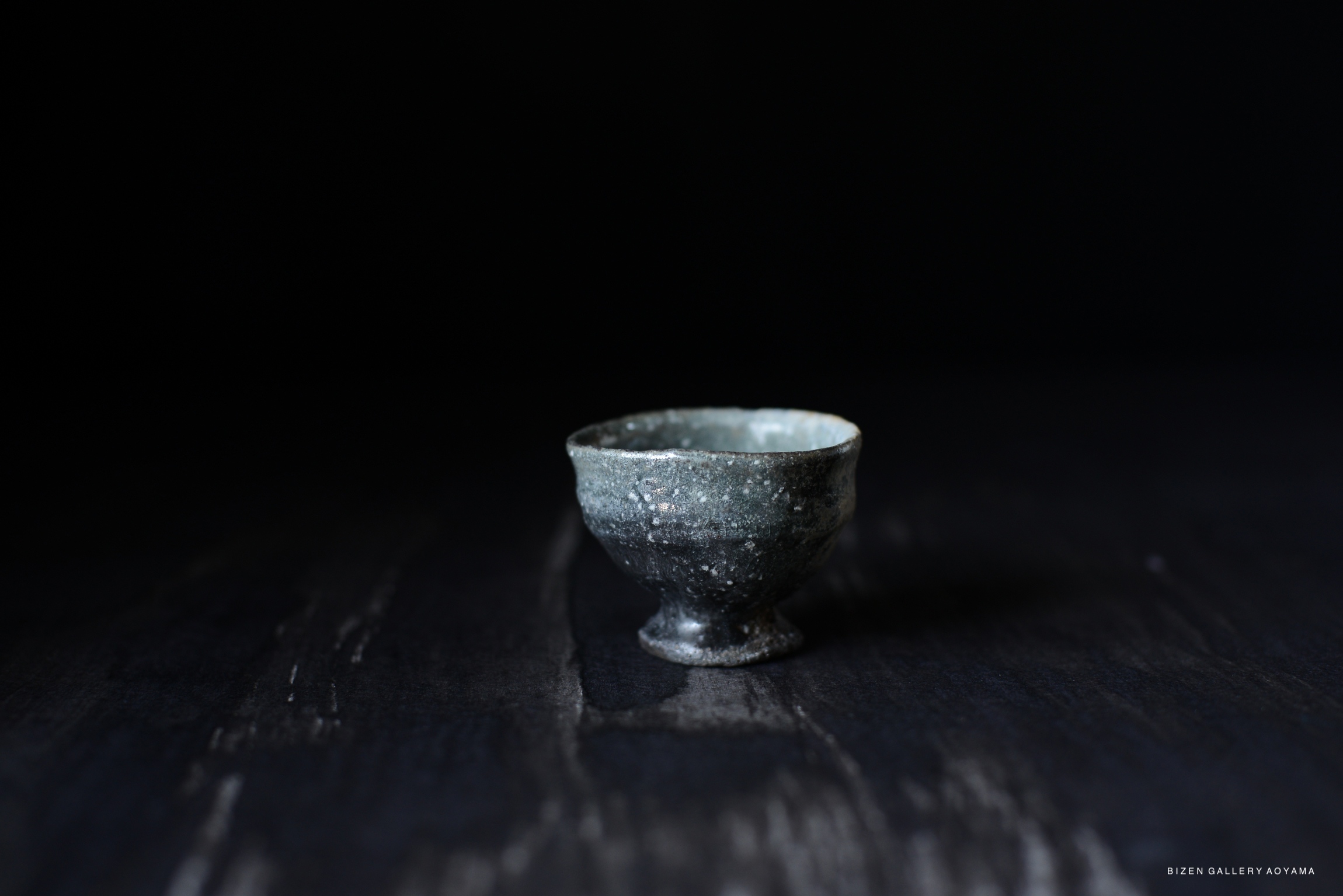 A small Iga drinking cup with a textured surface and a subtle sheen, set against a dark background.