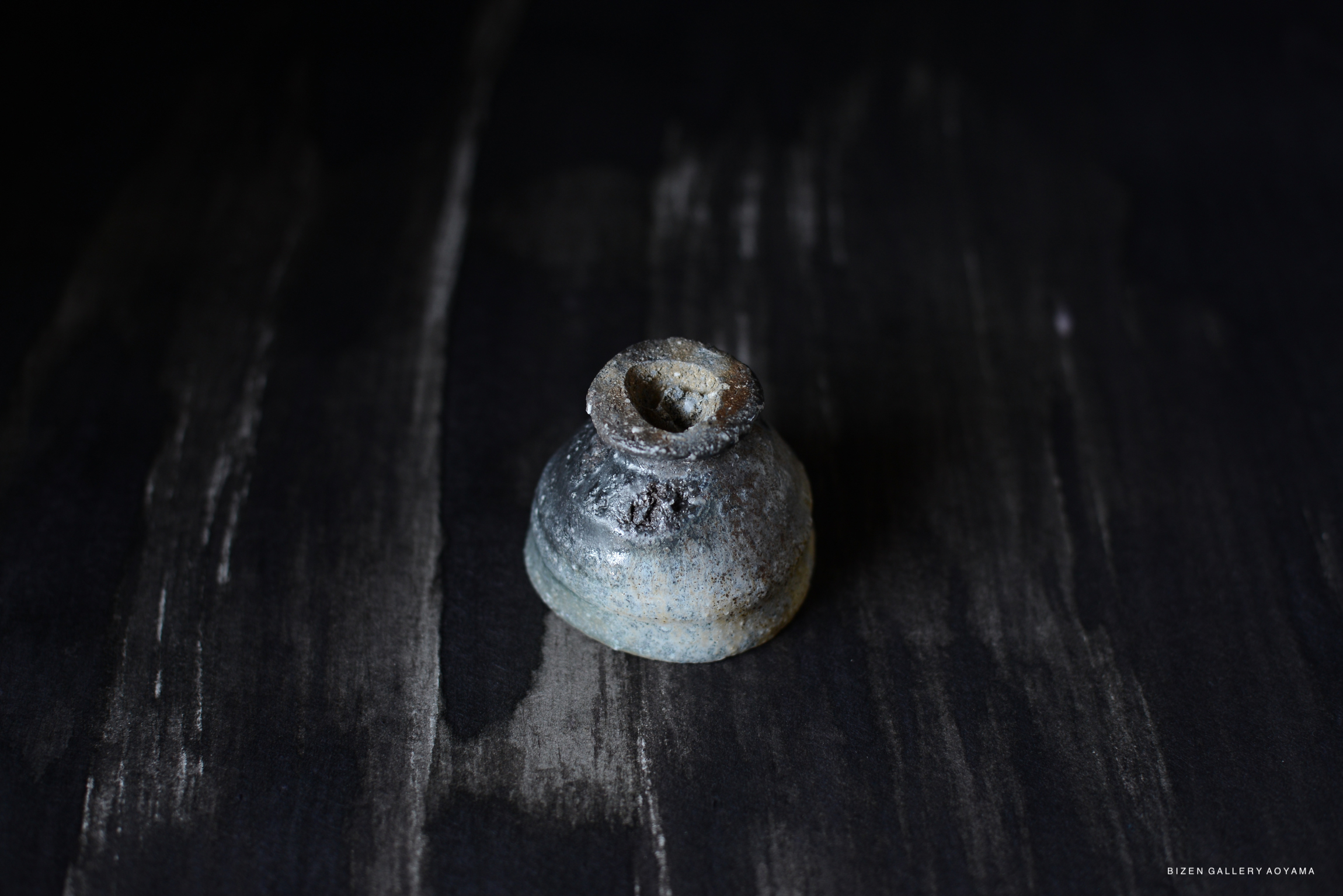 A small, hand-crafted Iga pot with a rounded base and a narrow neck, showcasing a rustic glaze on a dark wooden surface.