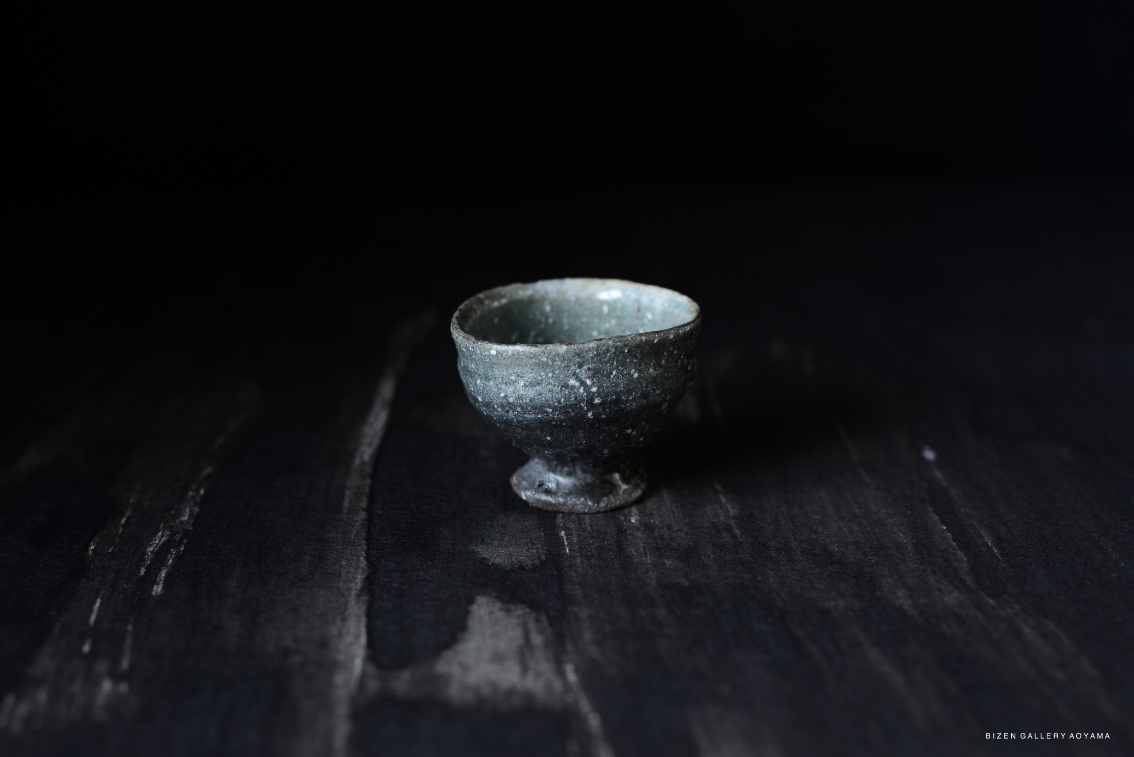 A small, dark ceramic bowl with a slightly flared rim, resting on a textured surface.