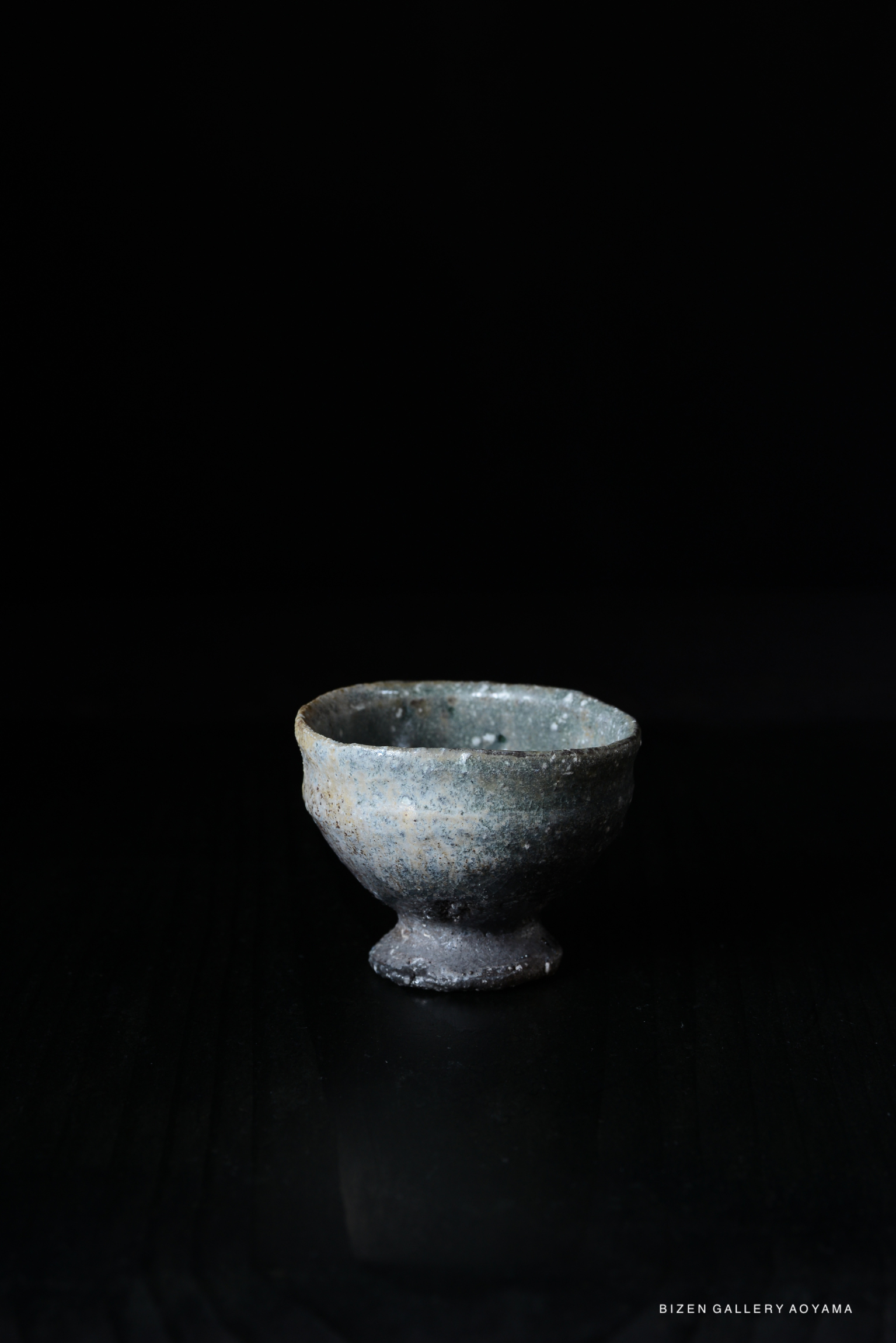 A dark, textured Iga-style guinomi with a rounded base, set against a black background.