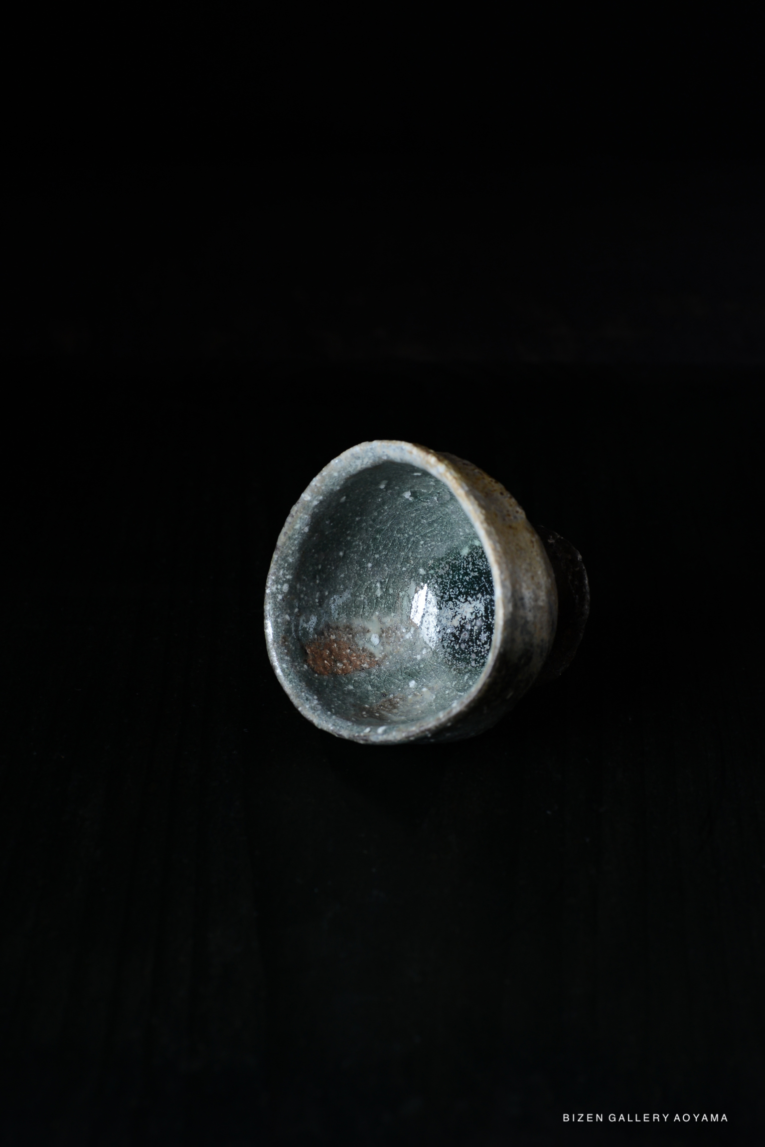 Iga-style handcrafted cup with a rustic glaze, showcasing unique textures and colors, displayed against a dark background.