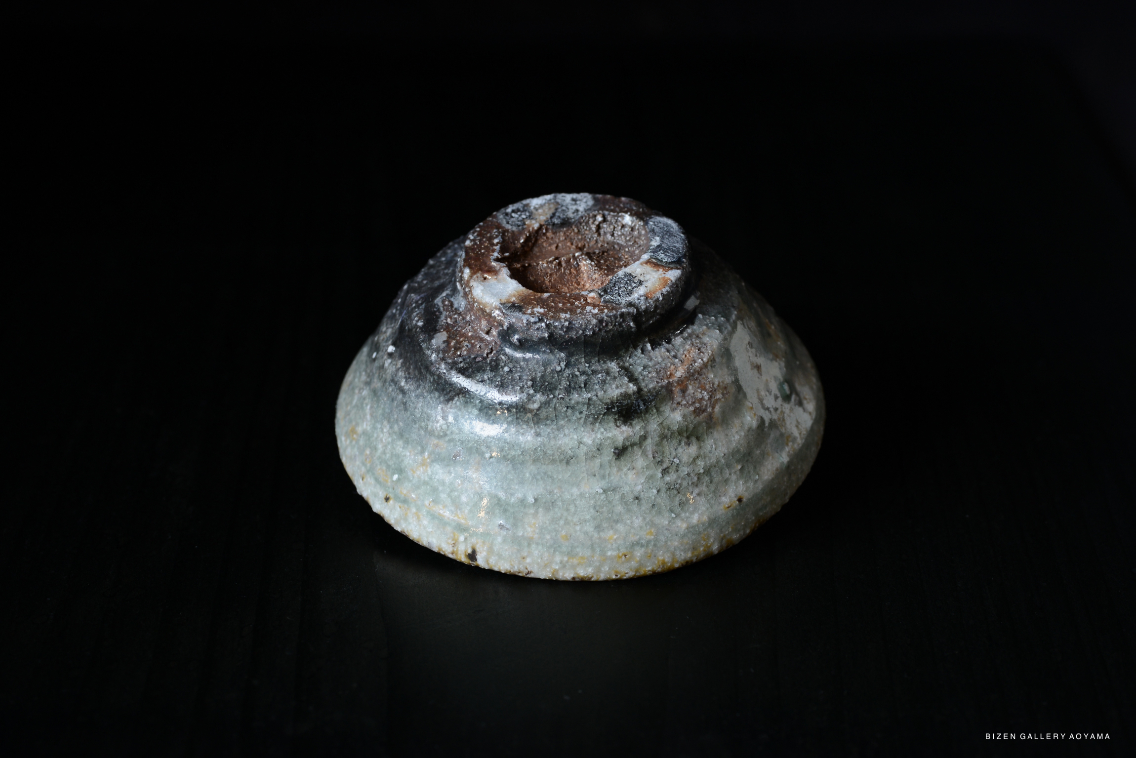 A close-up view of a handmade Iga-style pottery vessel with a textured surface and natural glaze variations. The piece is set against a dark background.
