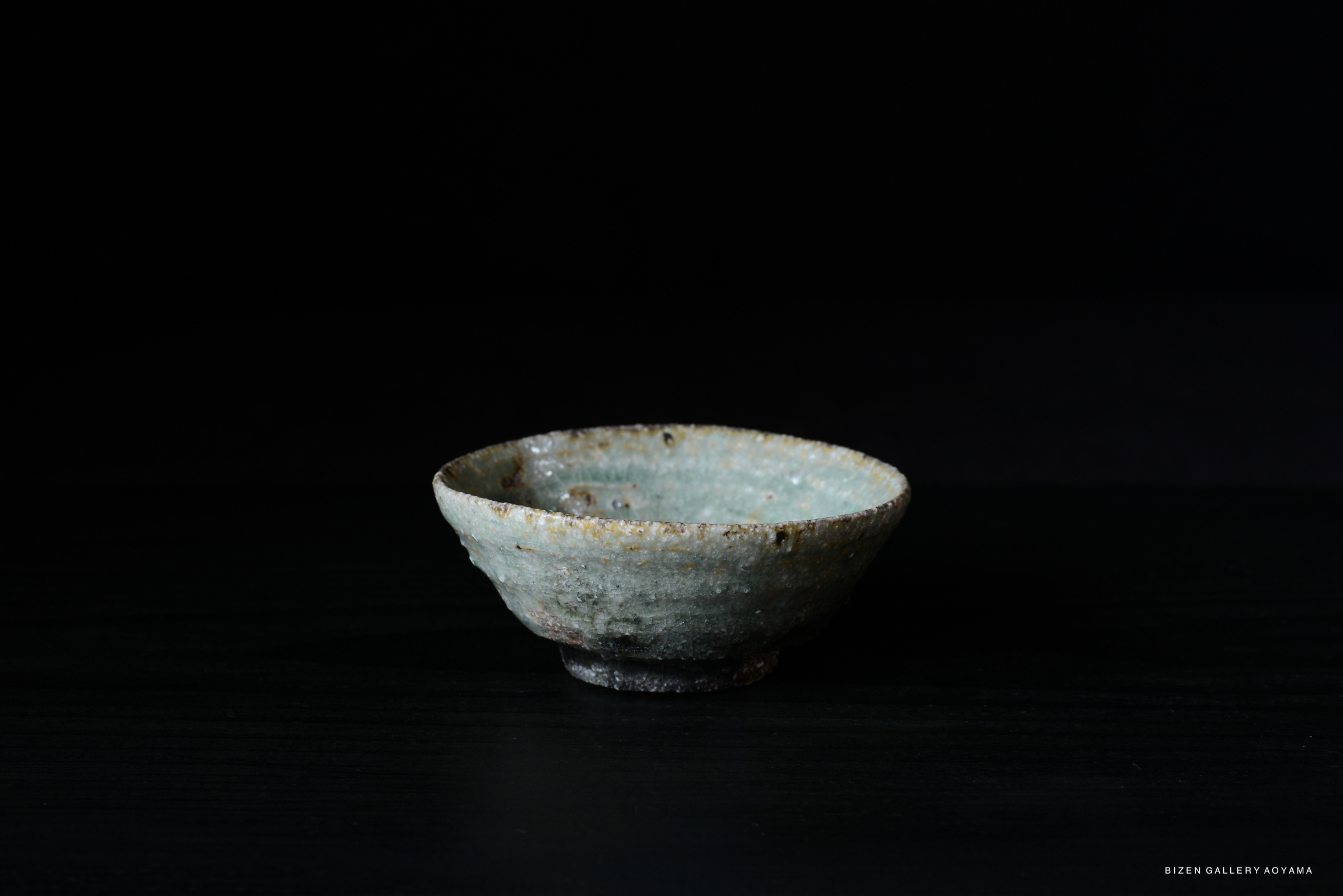 A handmade Iga ceramic bowl with a textured surface and subtle color variations, set against a dark background.
