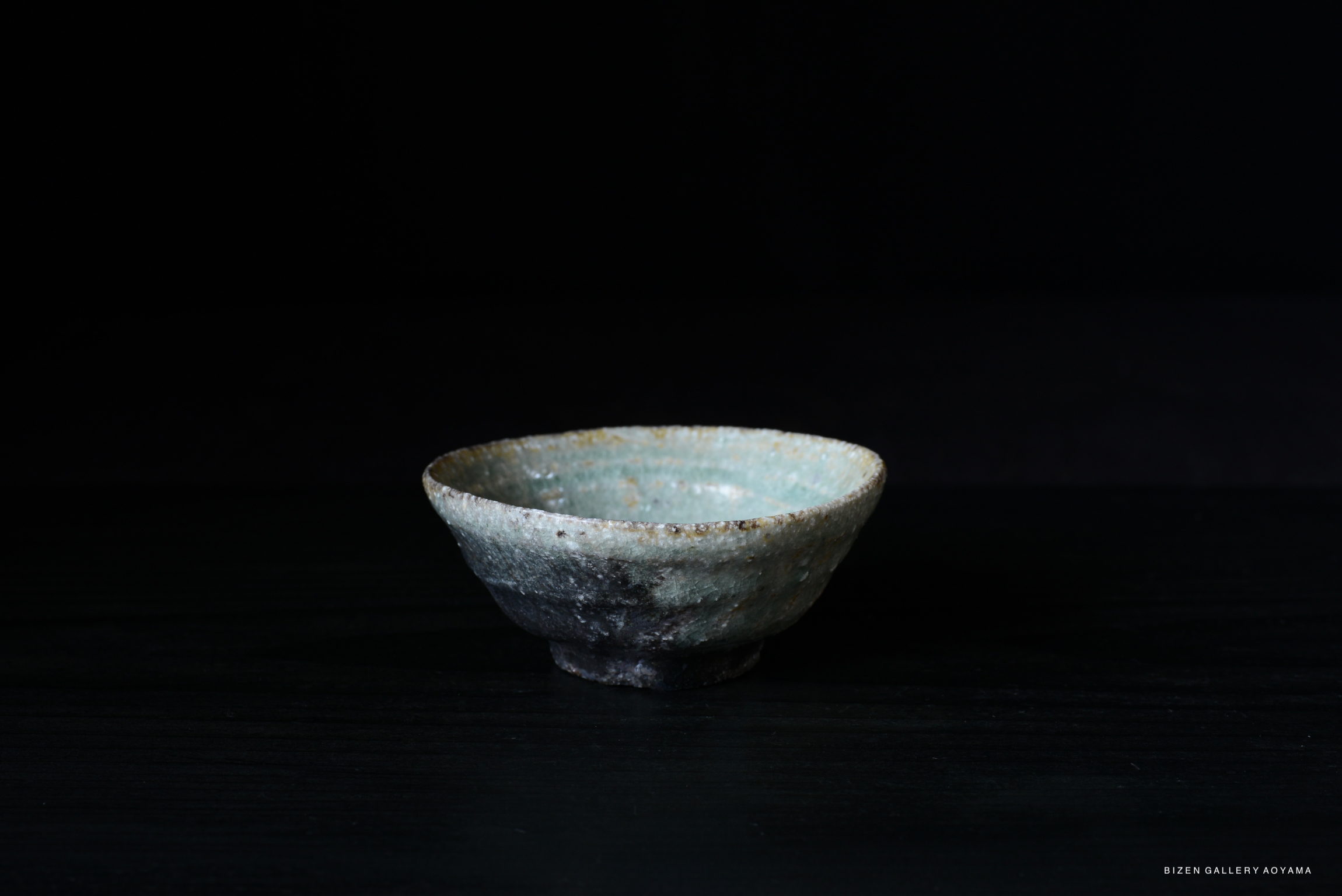 A handmade Iga pottery bowl with a textured surface and subtle glaze variations, displayed against a dark background.