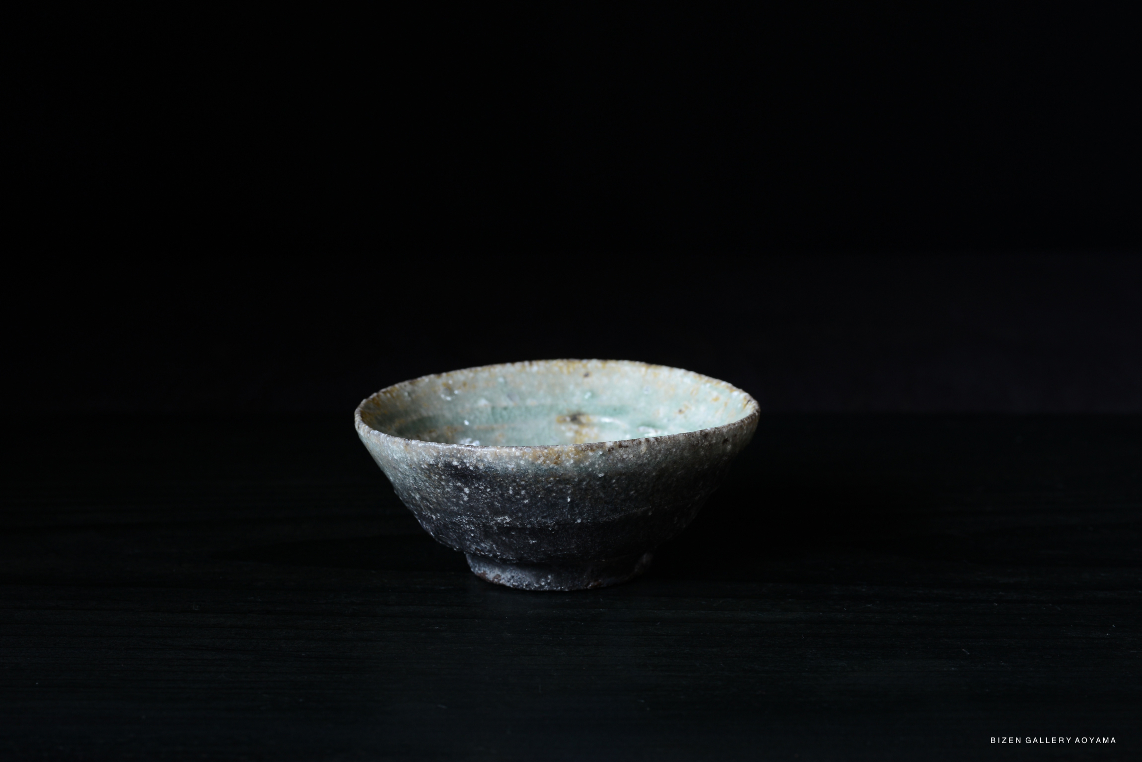 A rustic Iga pottery bowl with a textured surface, displaying shades of gray and light blue, set against a dark background.