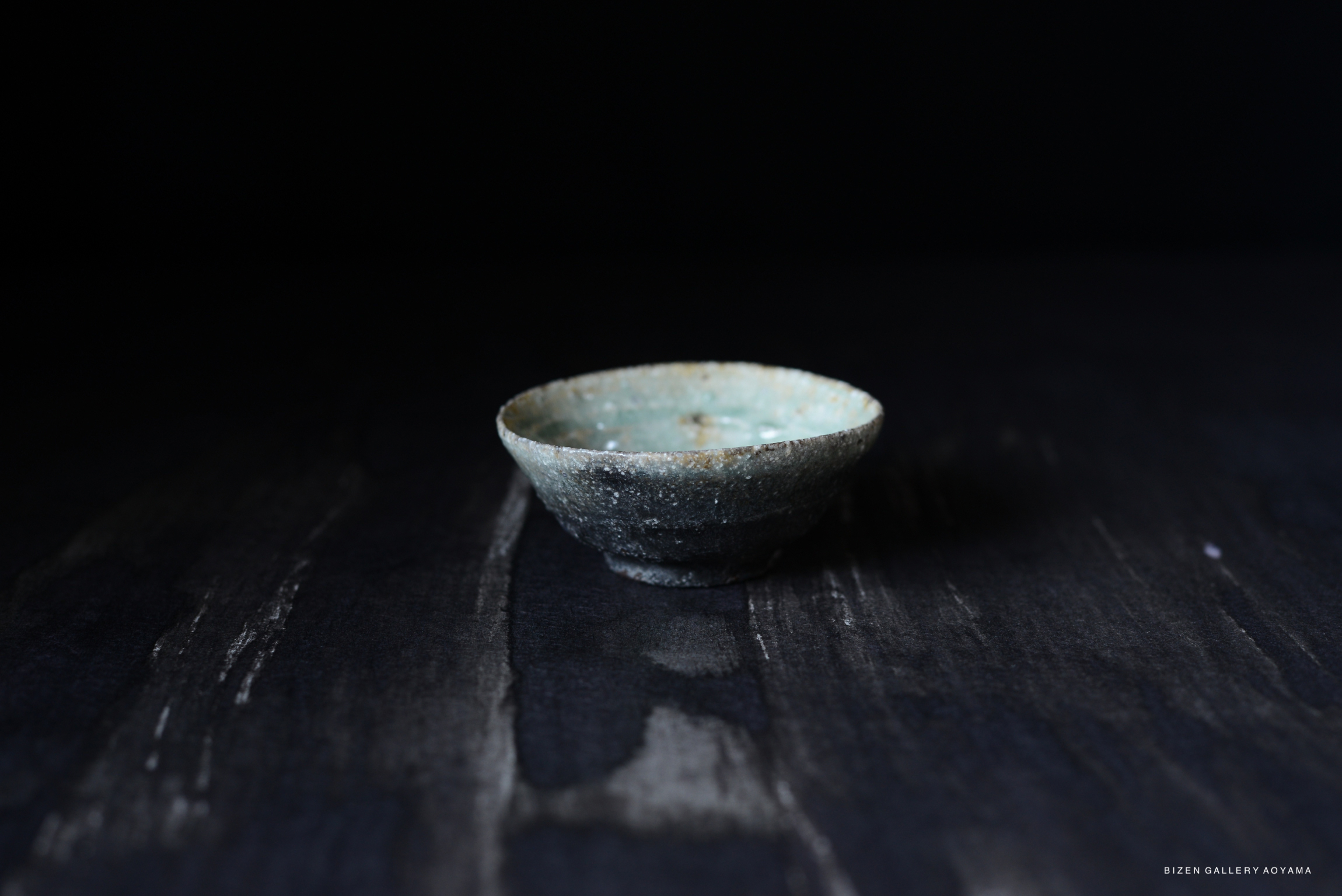 A textured, small Iga-style ceramic bowl with an earthy tone, displayed on a dark surface, showcasing its unique craftsmanship.