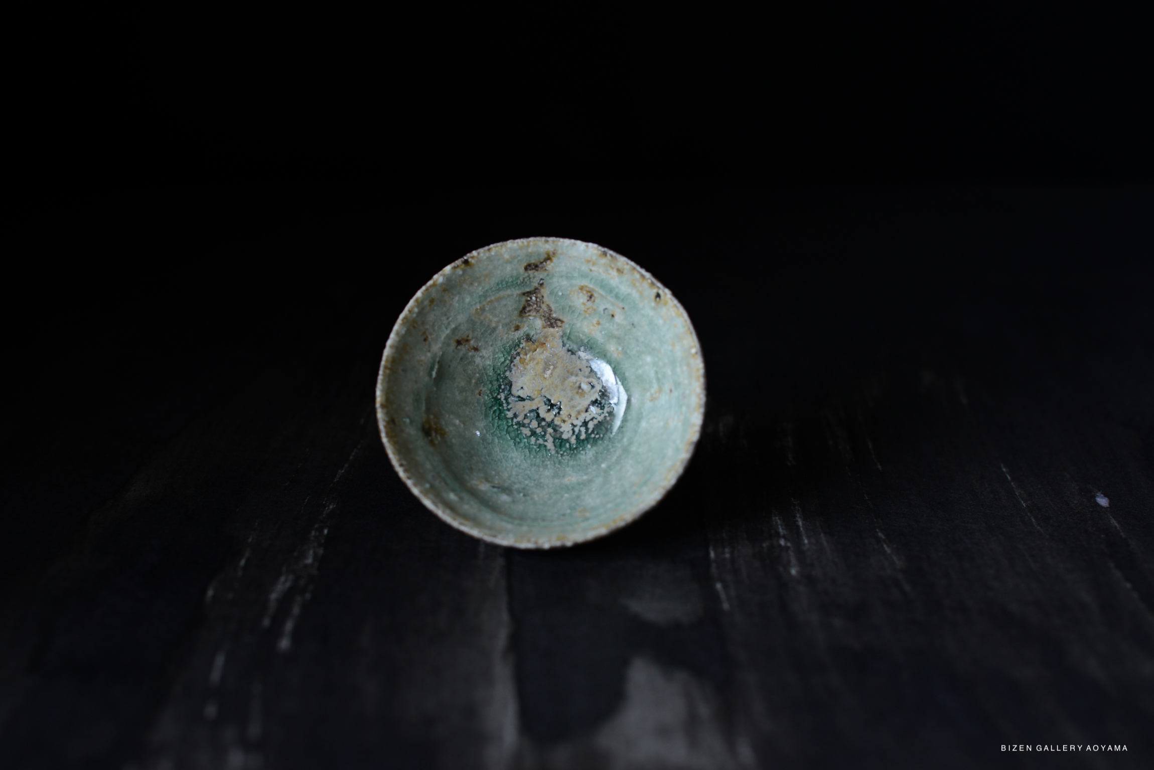 A top view of a small, light green ceramic bowl with a textured surface, displaying subtle imperfections and a faint glaze.