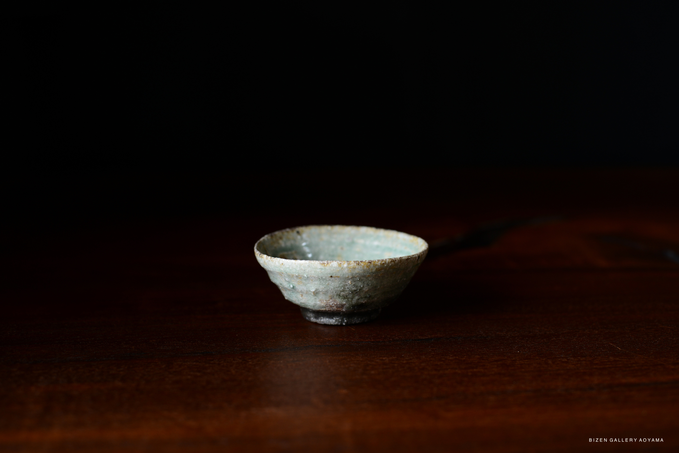 A small, handcrafted Iga-style bowl with a rustic texture and pale glaze, sitting on a wooden surface.