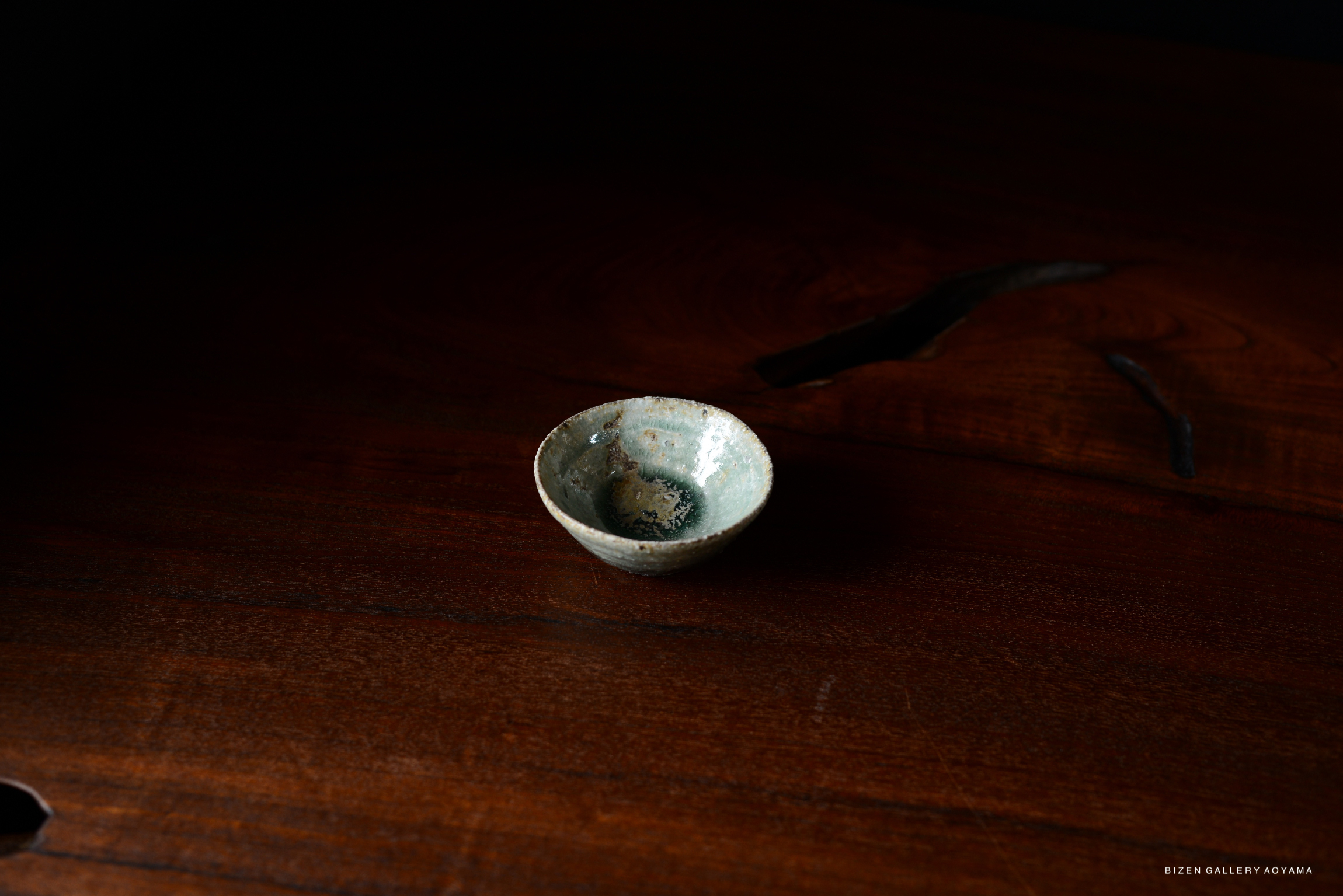 A small, round ceramic bowl with a light blue and green glaze, placed on a wooden surface.