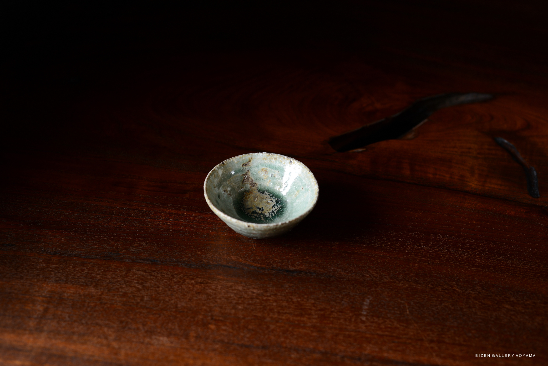 A handcrafted Iga-style bowl with a rustic green glaze on a dark wooden surface.