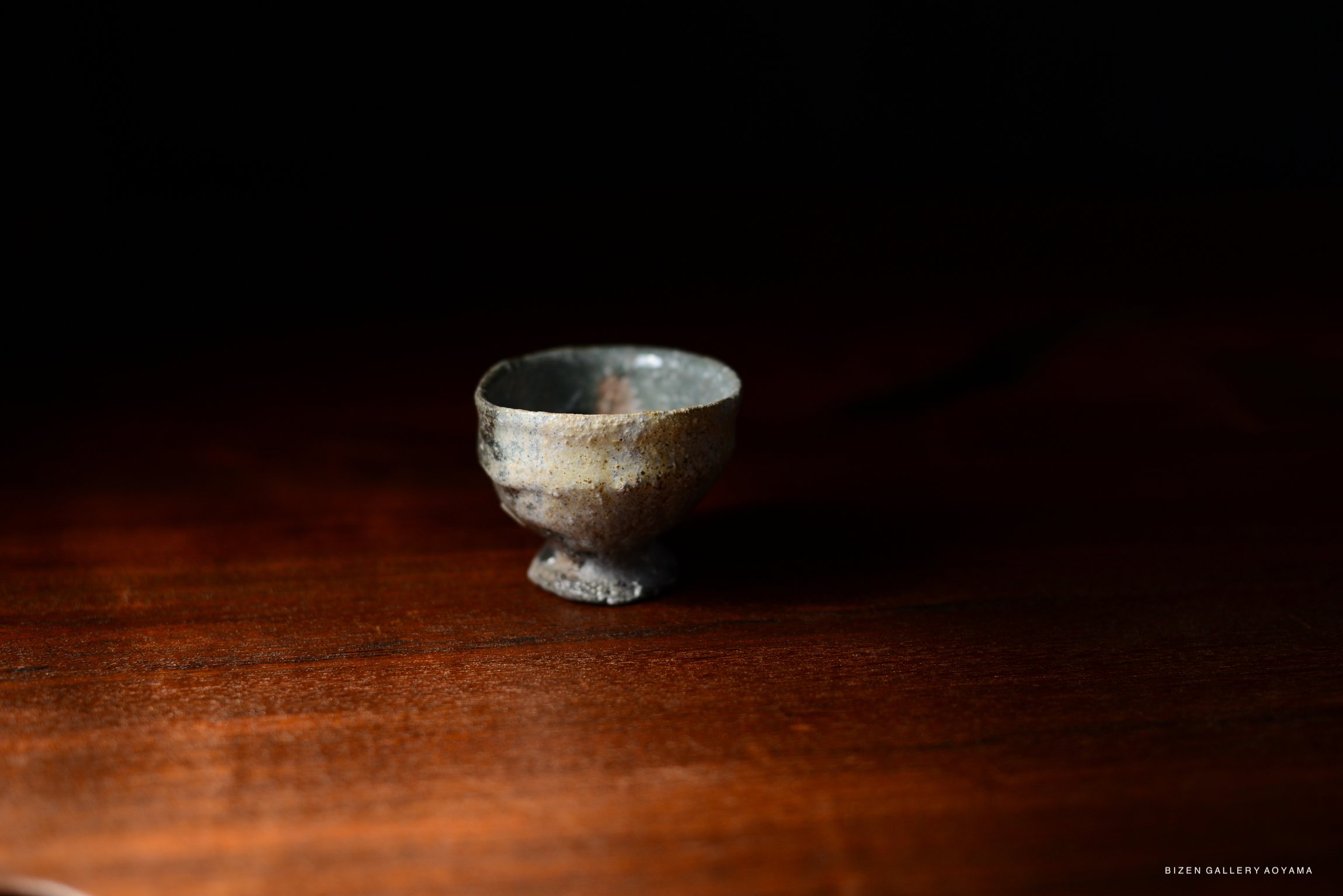 A small, textured Iga-style ceramic cup with a rustic finish, placed on a dark wooden surface.