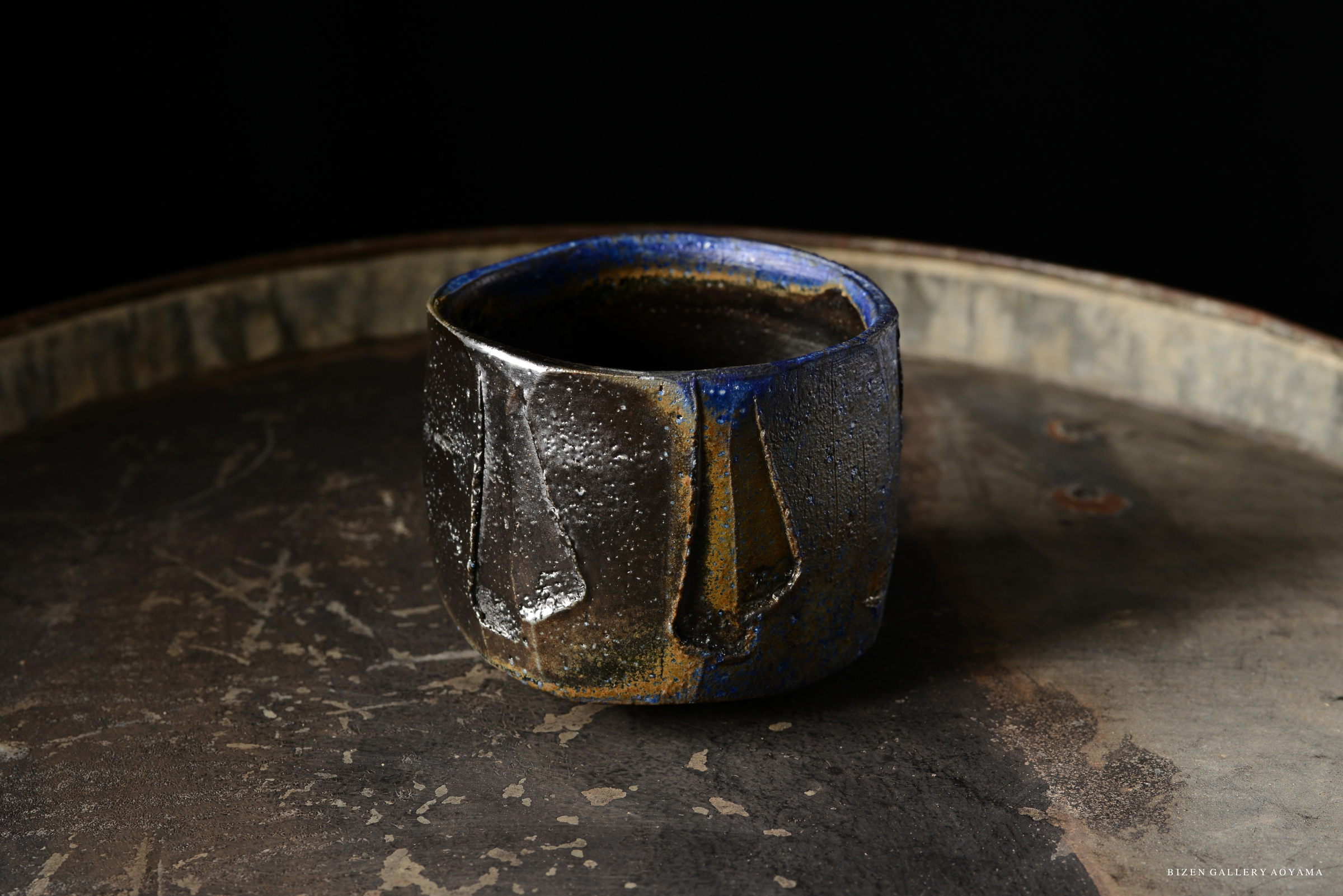 A close-up of a uniquely designed ceramic bowl with a textured surface and a blue rim, placed on a rustic metallic surface.
