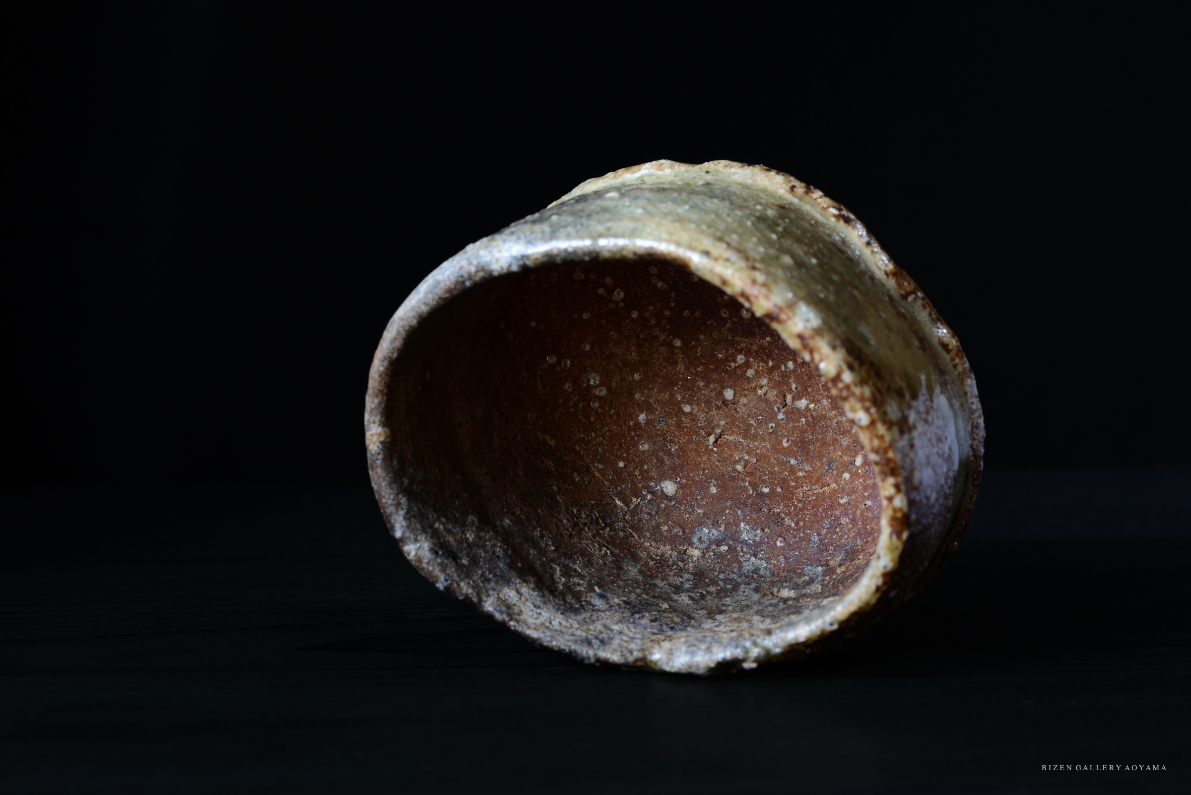 黒背景に置かれた、内側が茶色で外側に釉薬がかかった陶器のボウル