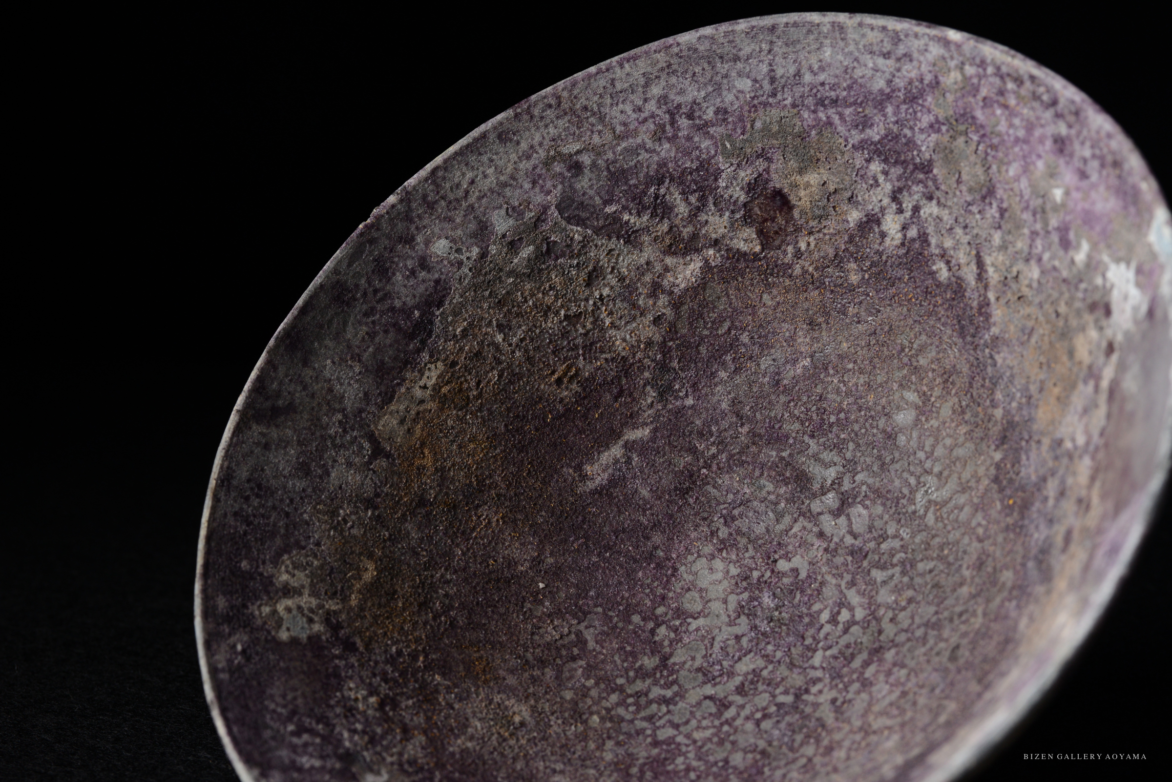 Close-up of a textured ceramic bowl with a purple surface, showcasing unique color variations.