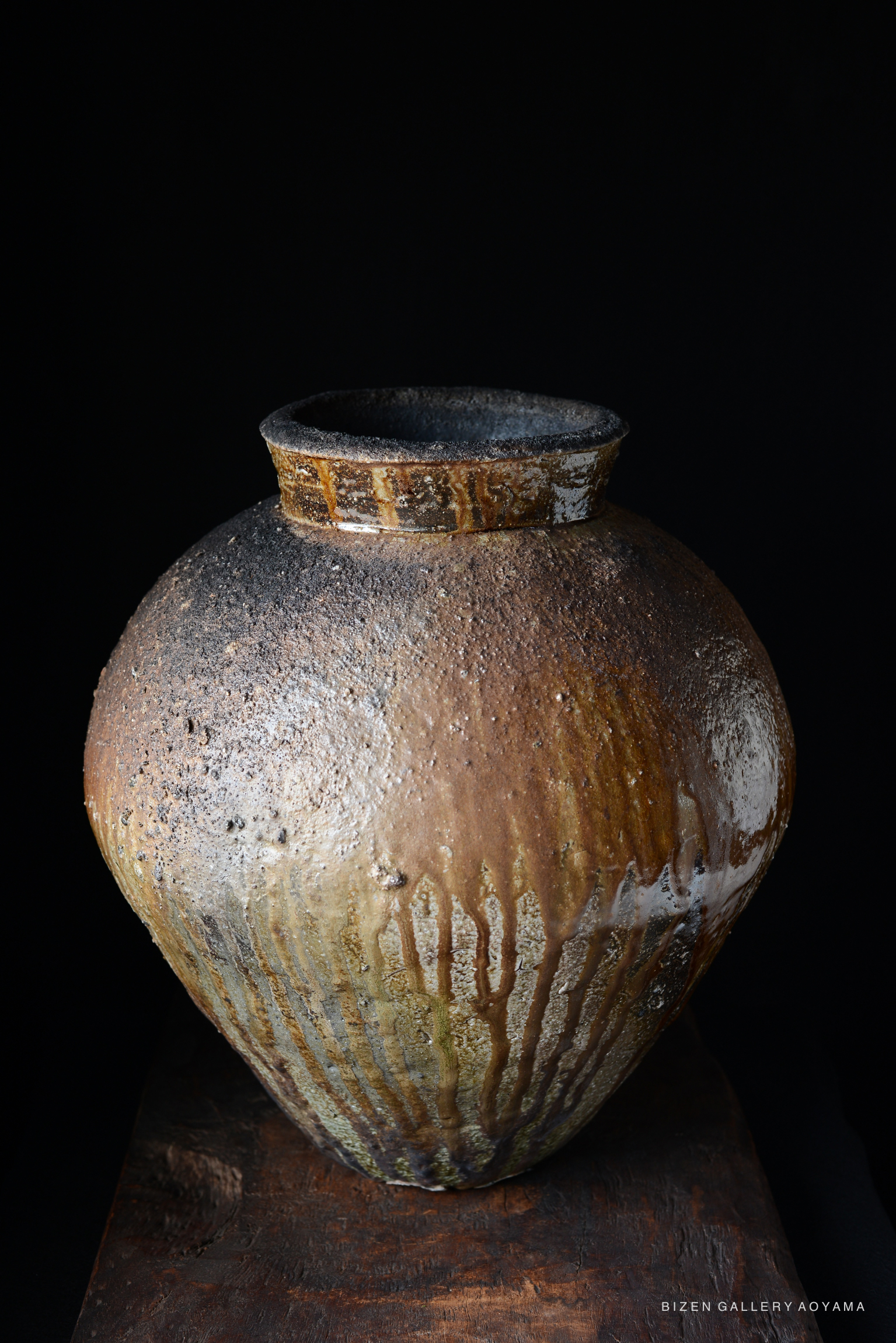 A close-up view of a traditional Bizen pottery jar, showcasing its textured surface and earthy tones against a dark background.