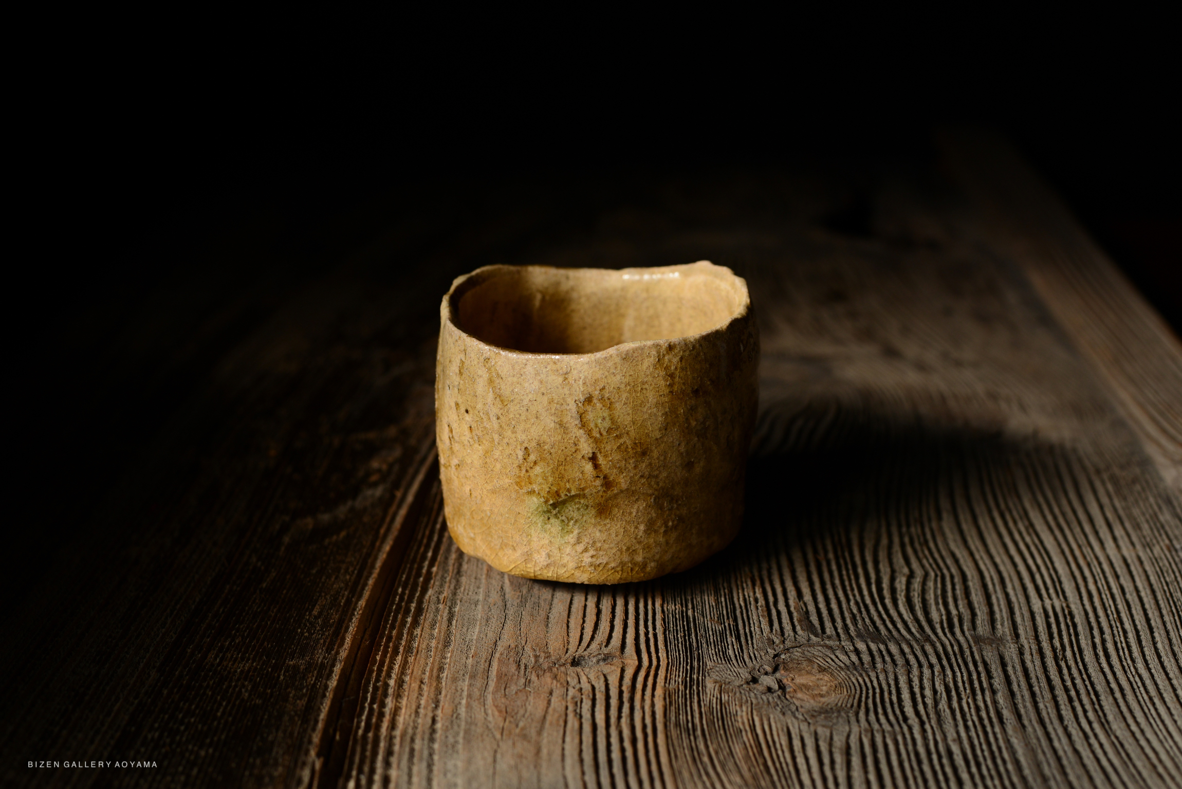 A close-up of a handcrafted ceramic cup placed on a wooden surface with a soft focus background.
