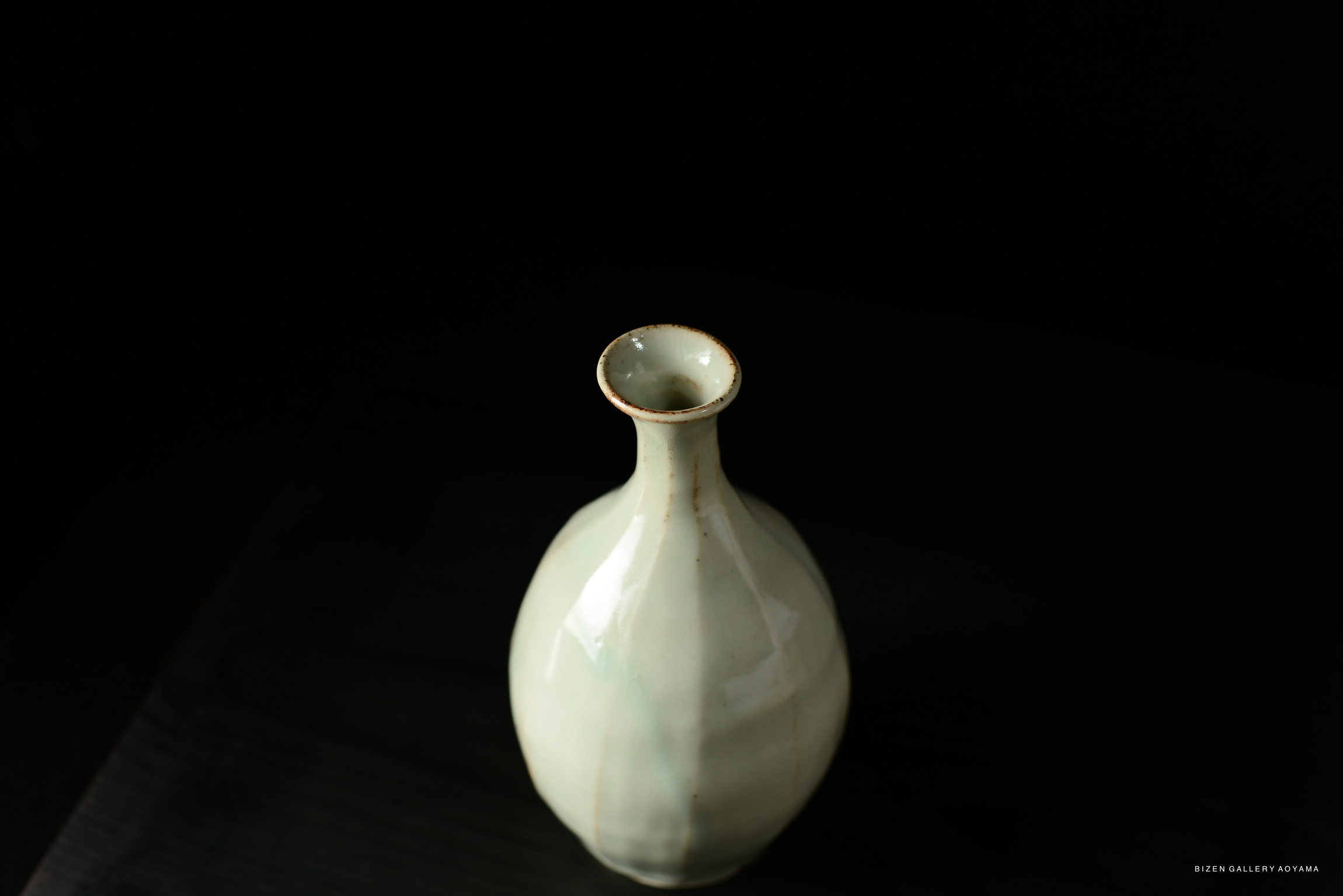 A top view of a delicate, pale ceramic vase with a slender neck and a rounded body, placed on a dark surface.
