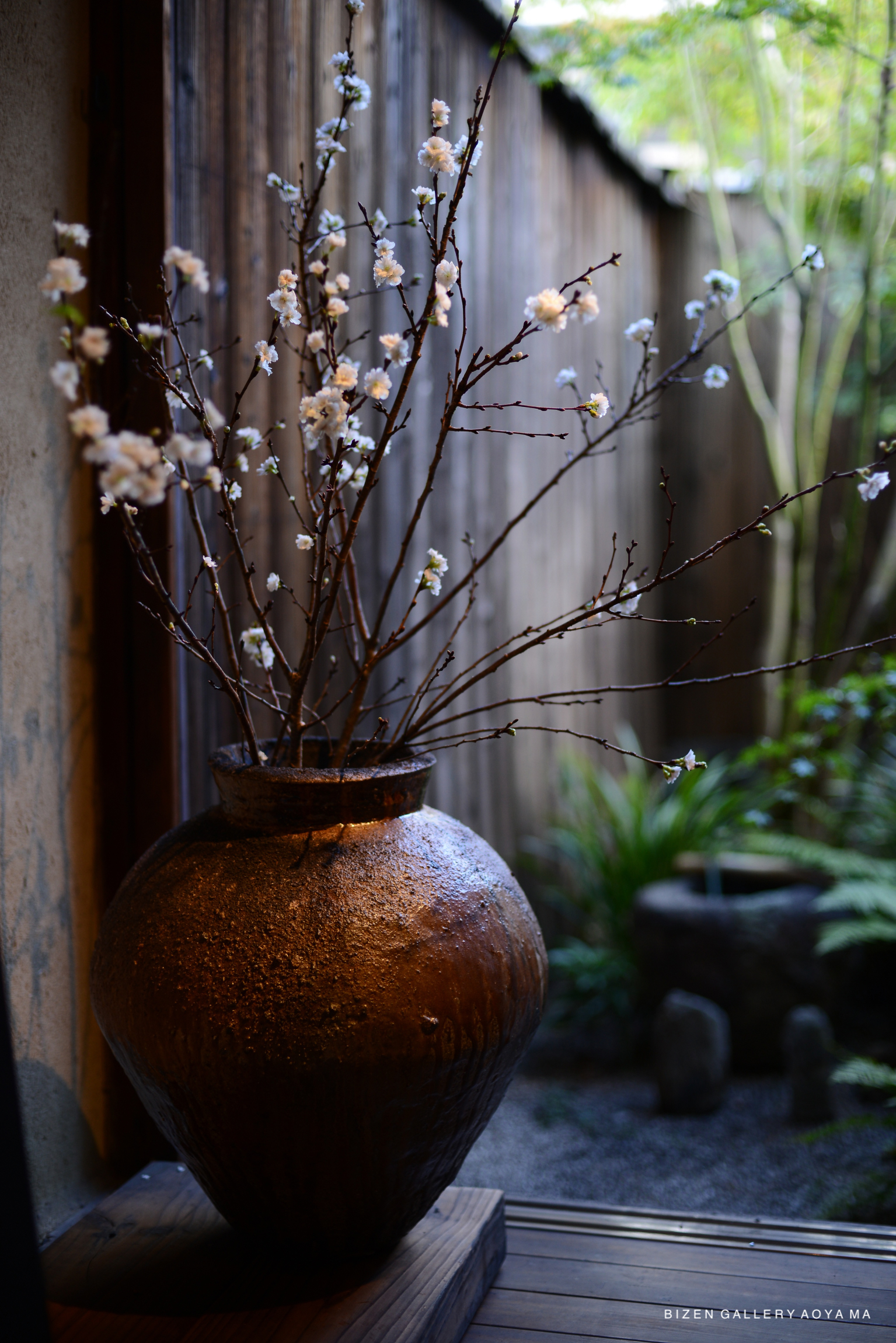 A Bizen pottery vase with flowering branches, placed in a serene indoor garden setting.