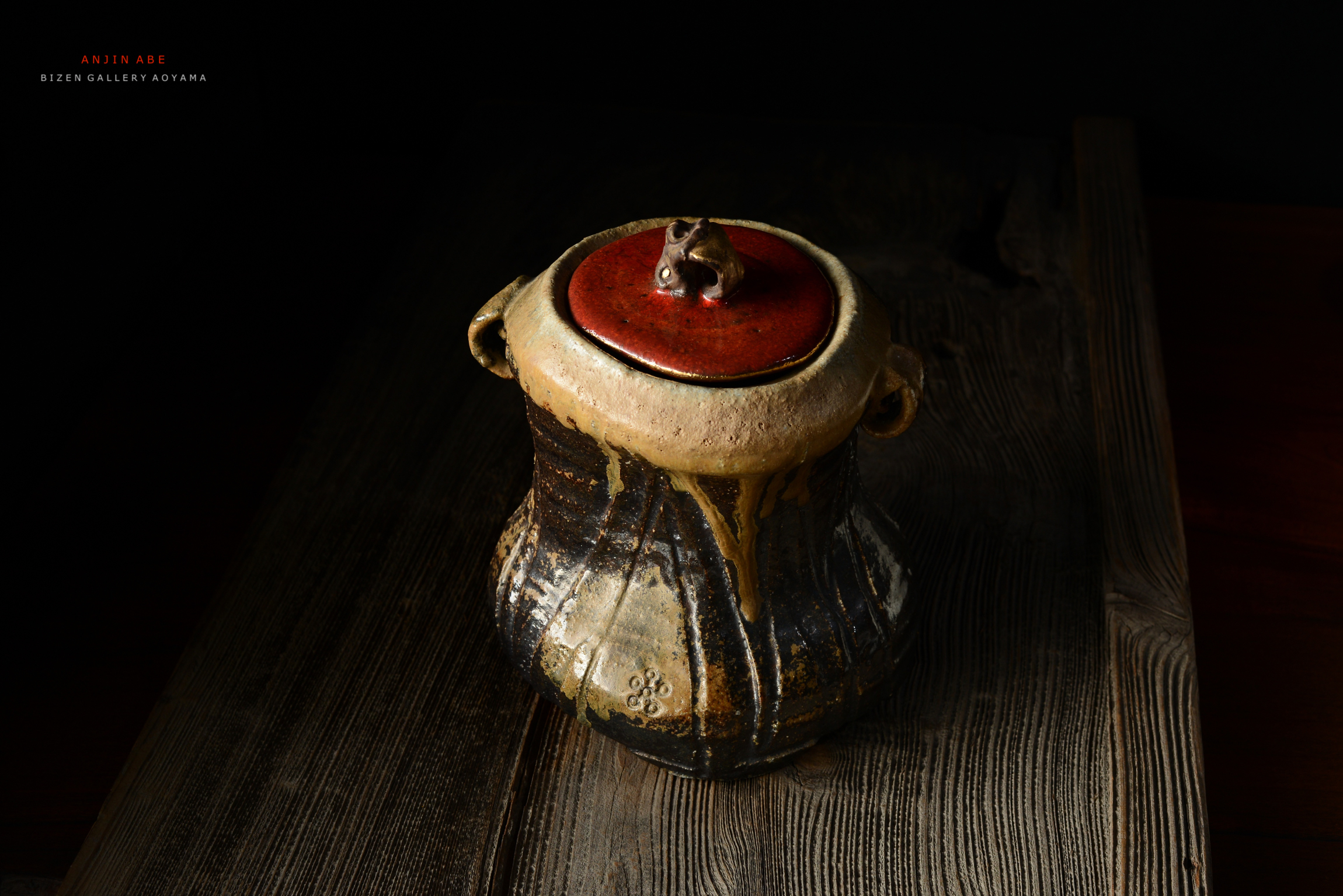 黒い背景に置かれた、赤いふたの陶器の壺。木のテーブルの上に設置されている。