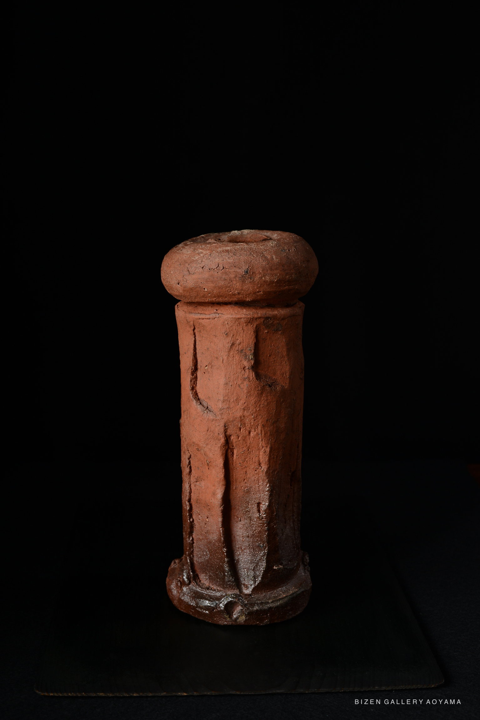 A tall decorative ceramic piece with a rounded top and textured surface, showcasing the rich earth tones typical of Bizen ware, set against a dark background.