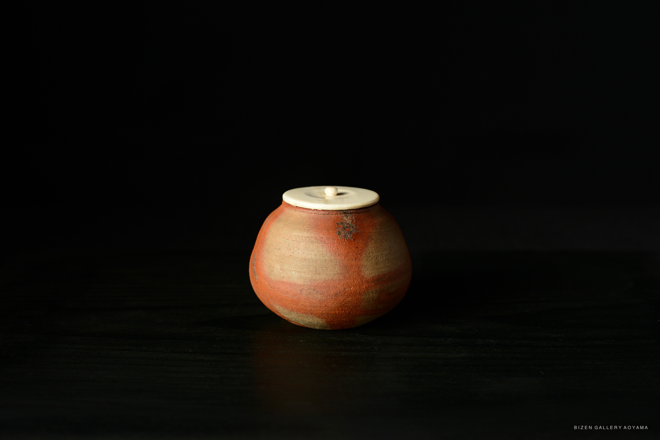 A traditional Japanese tea pottery piece, showcasing a rounded shape with a textured red and earthy finish, and a white lid on top.