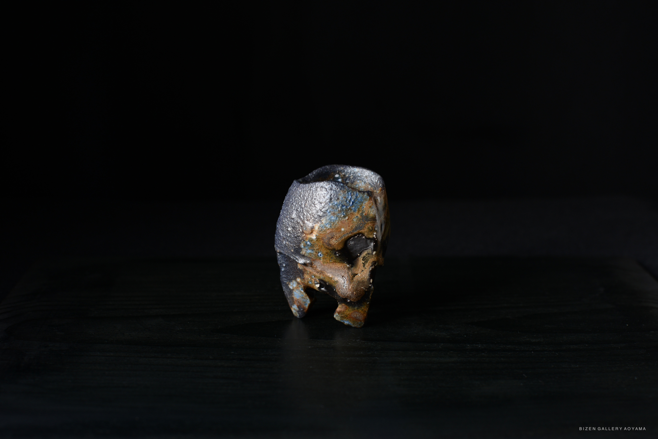 A unique Bizen ware ceramic piece, showcasing a blend of colors and textures, with a distinctive shape and intricate surface details, set against a dark background.