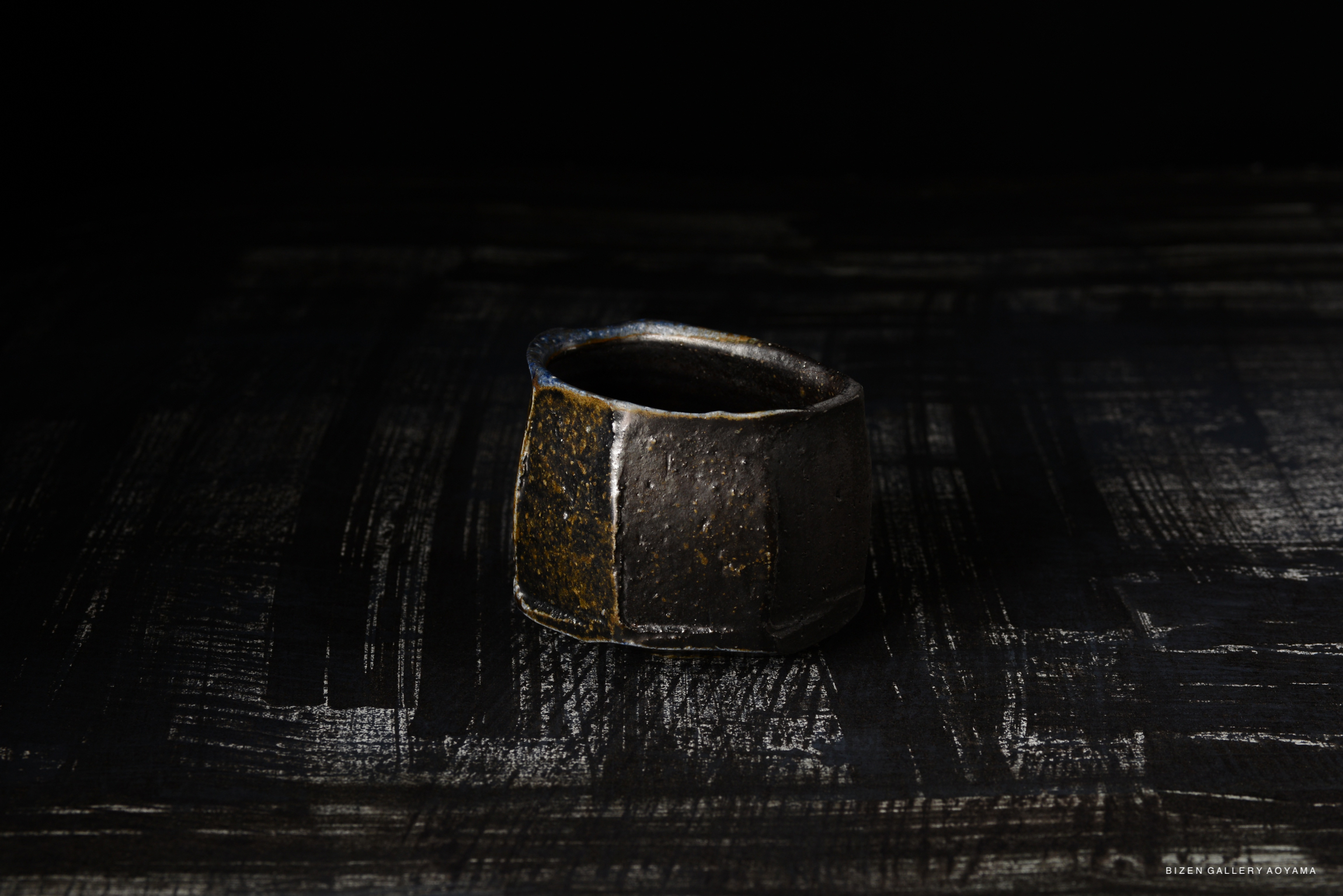 A dark, textured ceramic Kofuku Wan (small bowl) with a slightly irregular shape, showcased against a dark background.