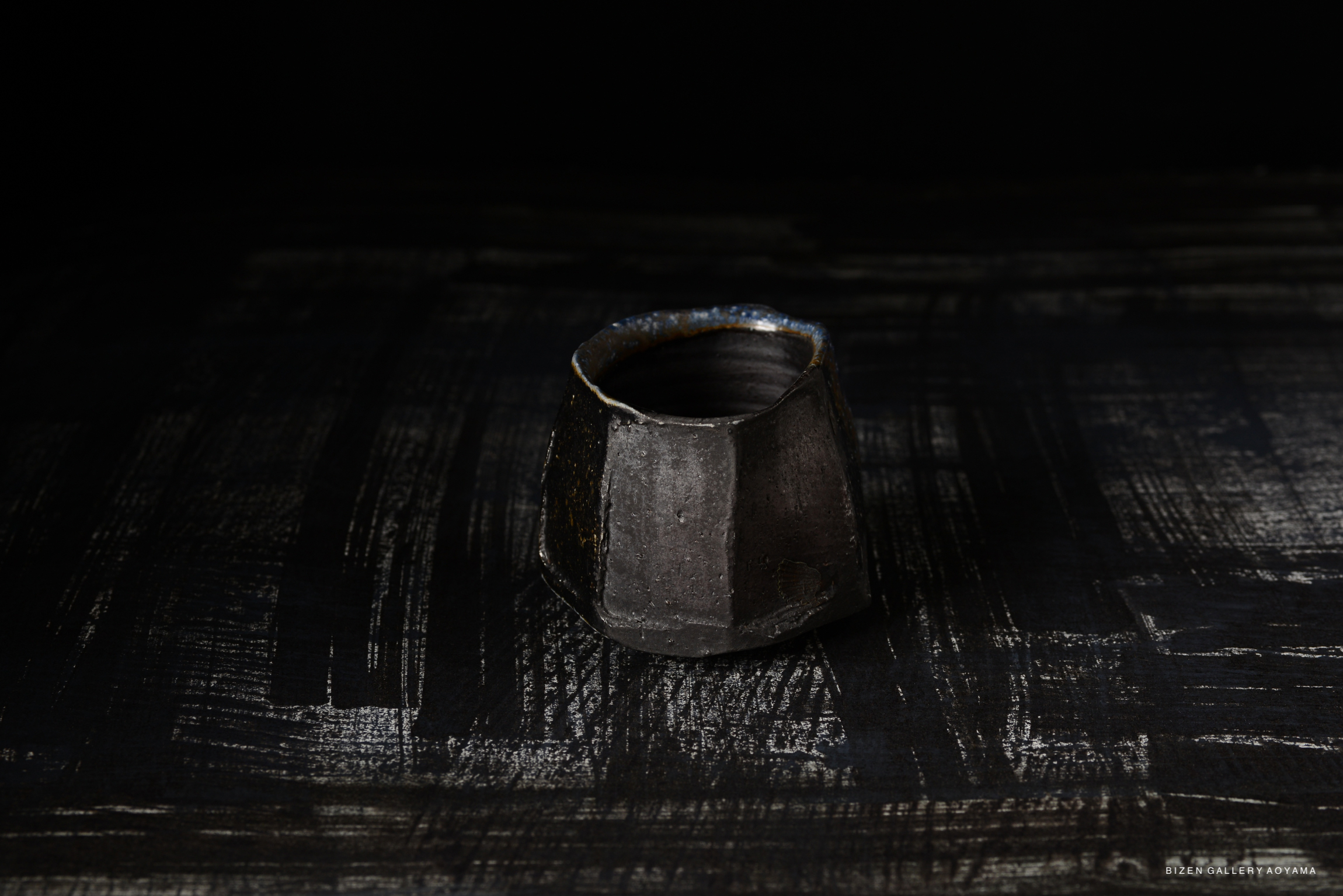 A close-up of a Bizen pottery Kofuku Wan, featuring a unique textured surface and dark coloration, set against a black background.