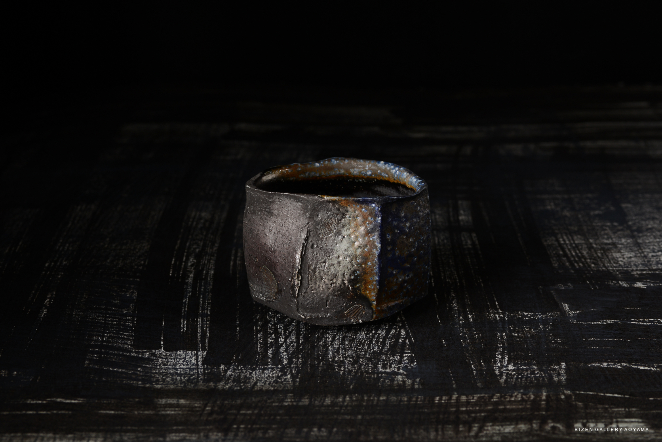 A Bizen pottery Kofuku Wan (small bowl) displayed against a dark background, showcasing its earthy textures and colors.