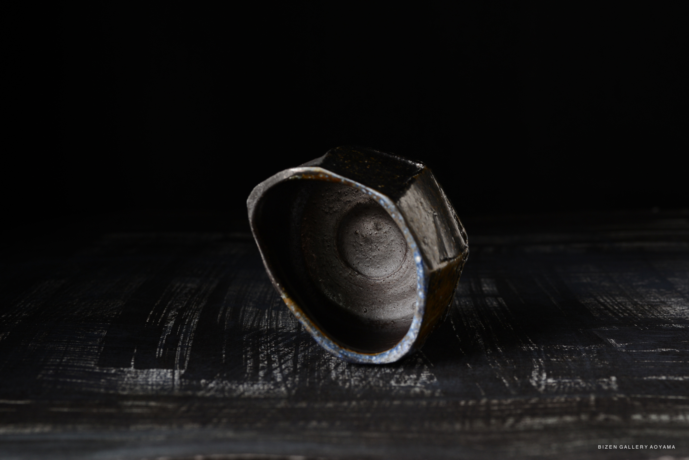 A close-up view of a Bizen Kofukuwan bowl, showcasing its unique, textured surface and hexagonal shape, set against a dark background.