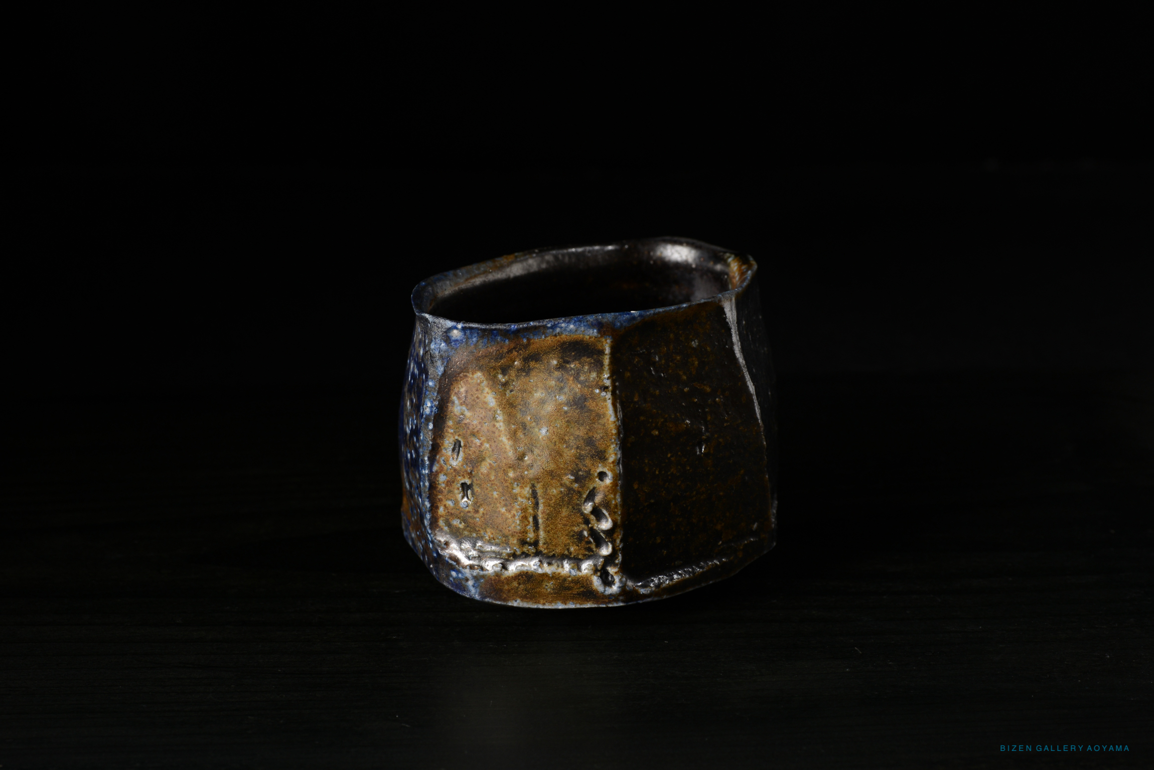 A close-up view of a Bizen pottery Kofuku Wan (small bowl) with a textured surface and earthy tones, displayed against a dark background.