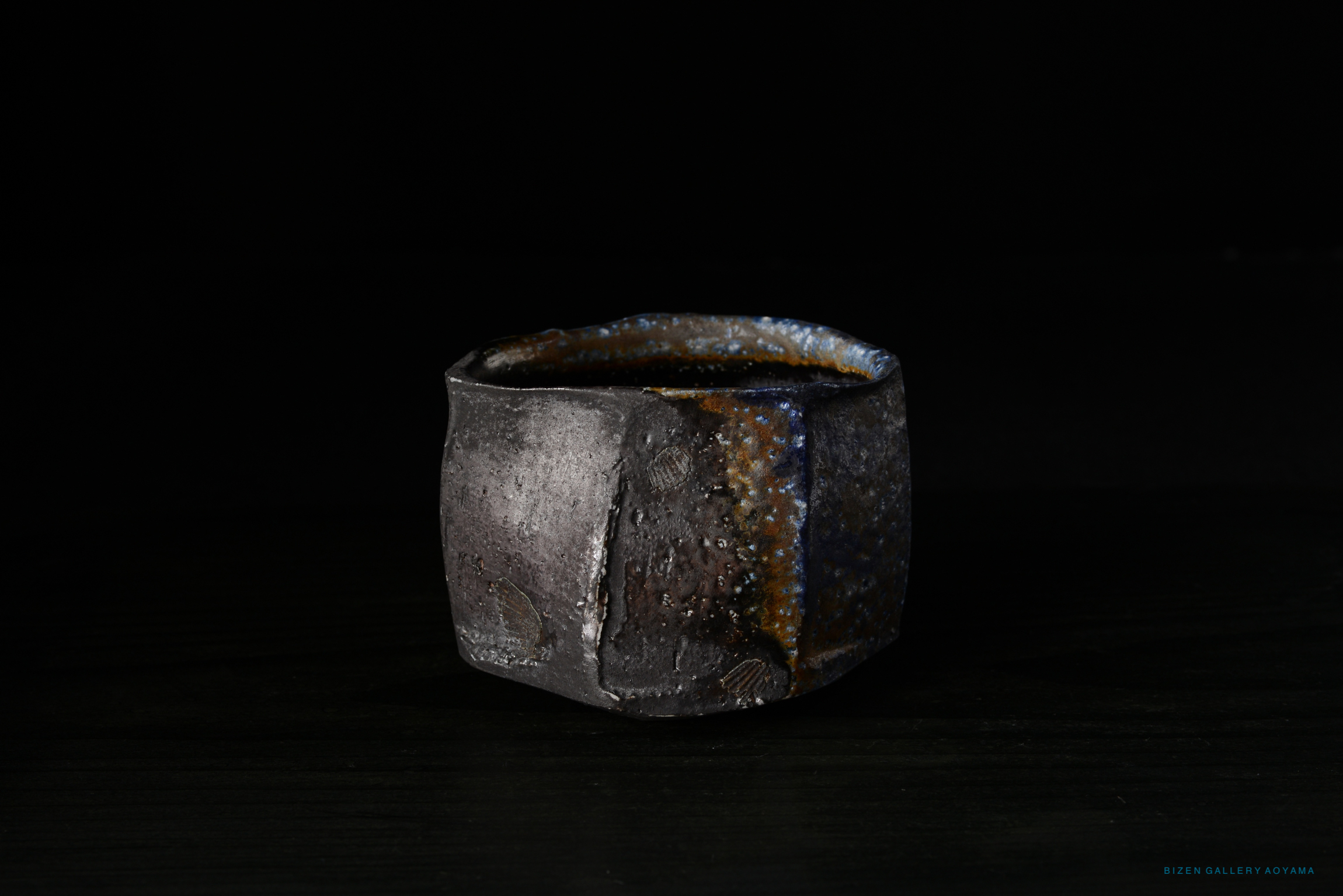A Bizen ceramic Kofuku Wan (小服碗) with a unique textured surface and earthy tones, displayed against a dark background.