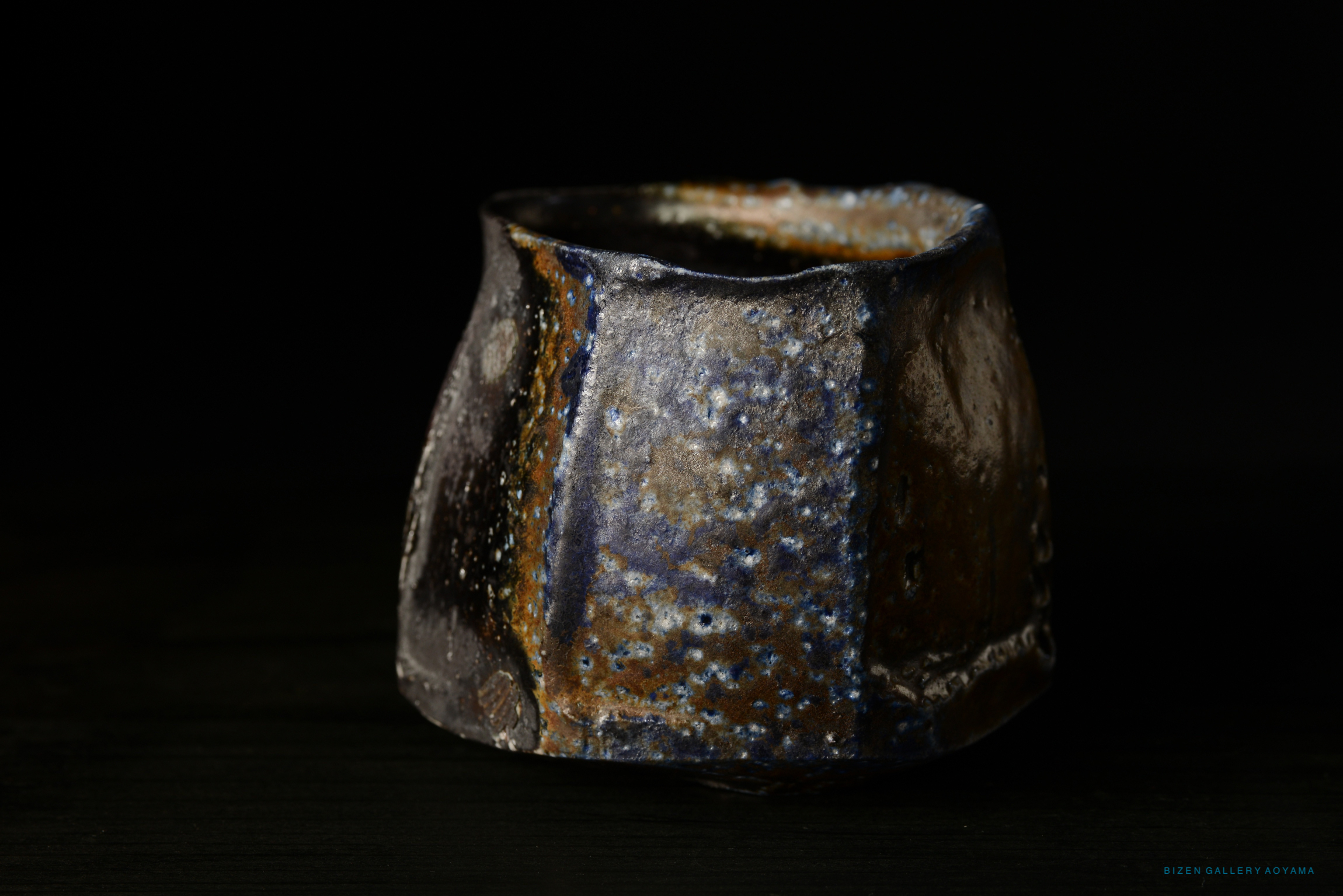 The image shows a textured Bizen pottery bowl with a unique brown and blue glaze, set against a dark background.