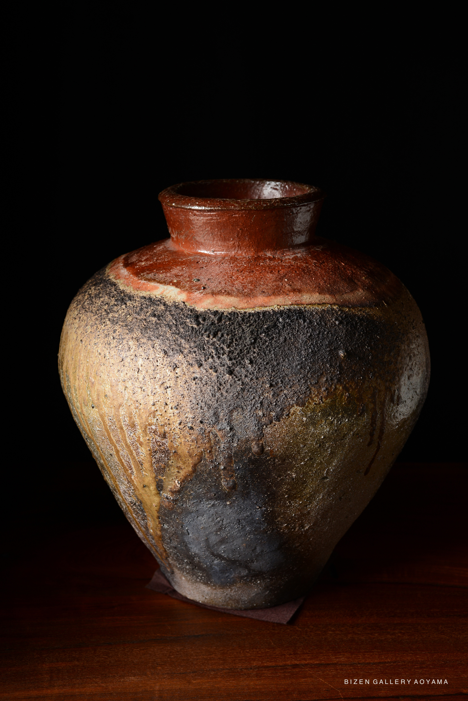 A Bizen tsubo pottery vase featuring a textured surface with a blend of earthy colors including brown, black, and yellow, set against a dark background.