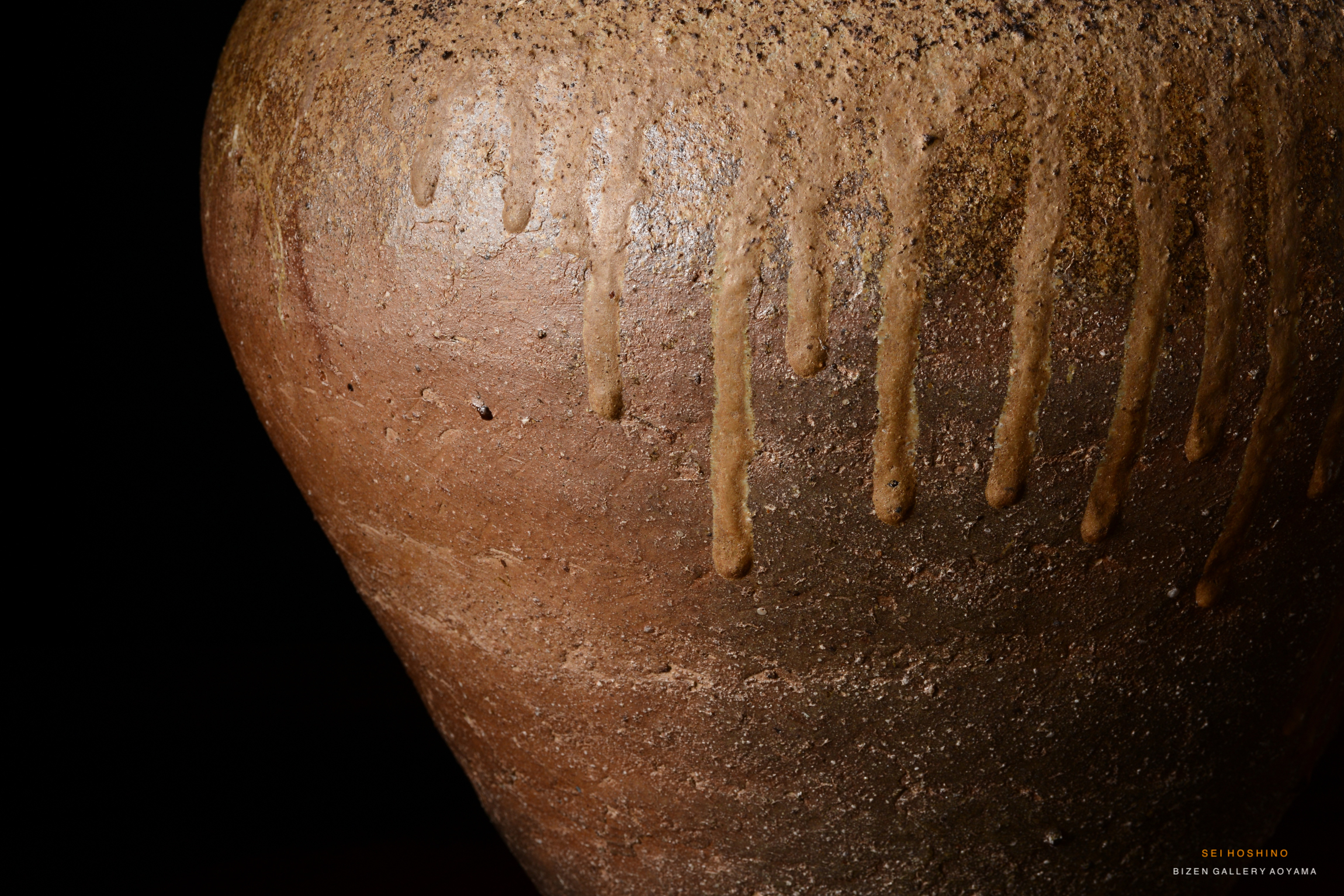 Close-up of a Bizen pottery jar showing drips and texture on its surface, with a dark background.