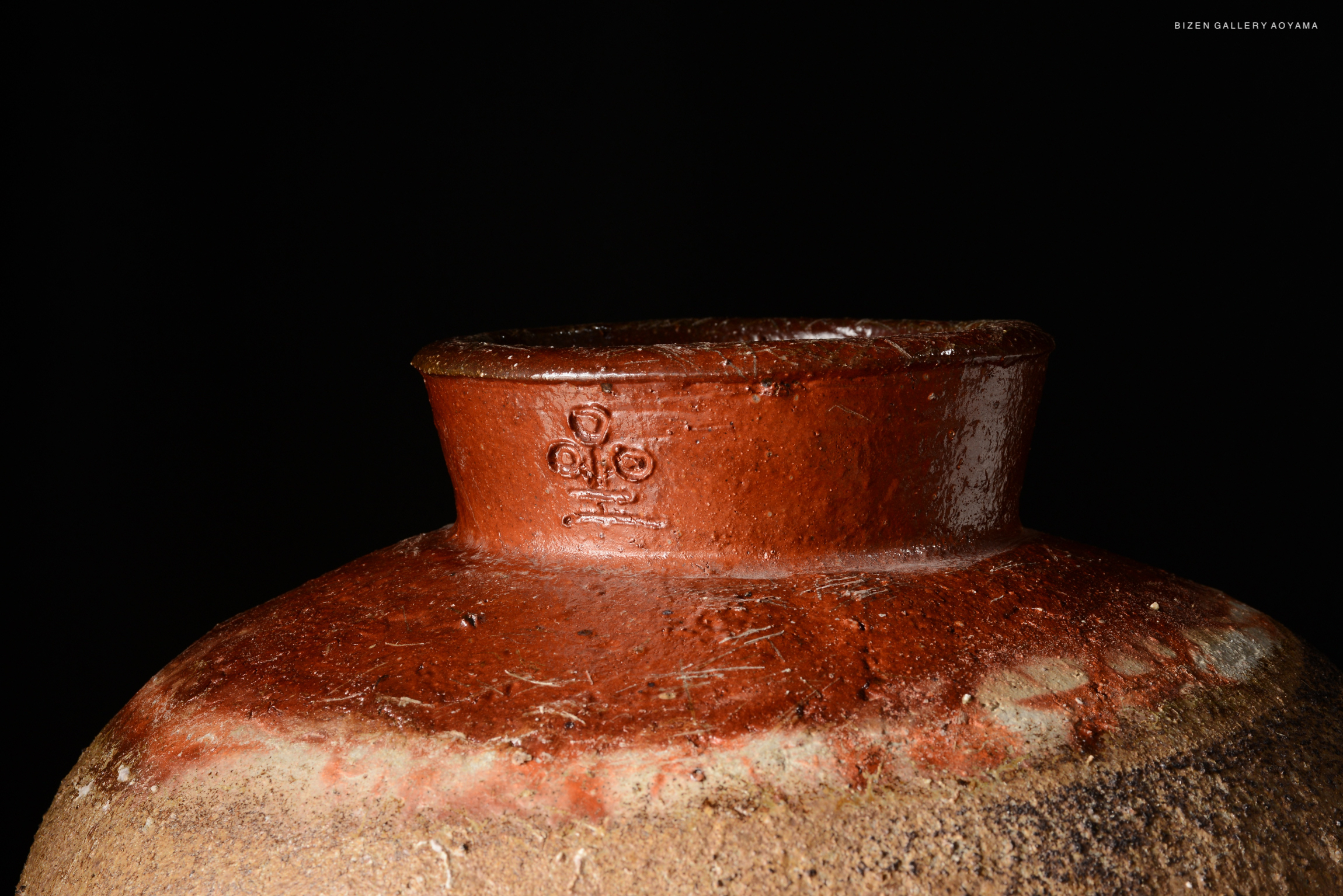 Close-up of the top of a Bizen tsubo, showcasing its distinctive round neck and textured surface against a dark background.