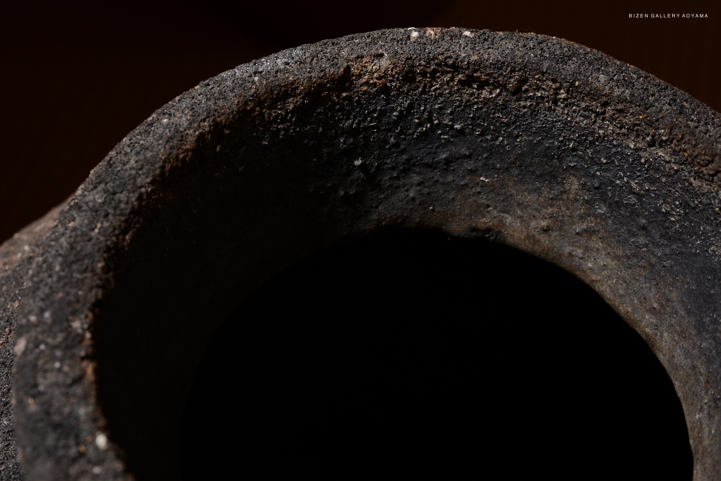 Close-up view of the rim of a Bizen pottery vessel, showing its textured surface and dark interior.