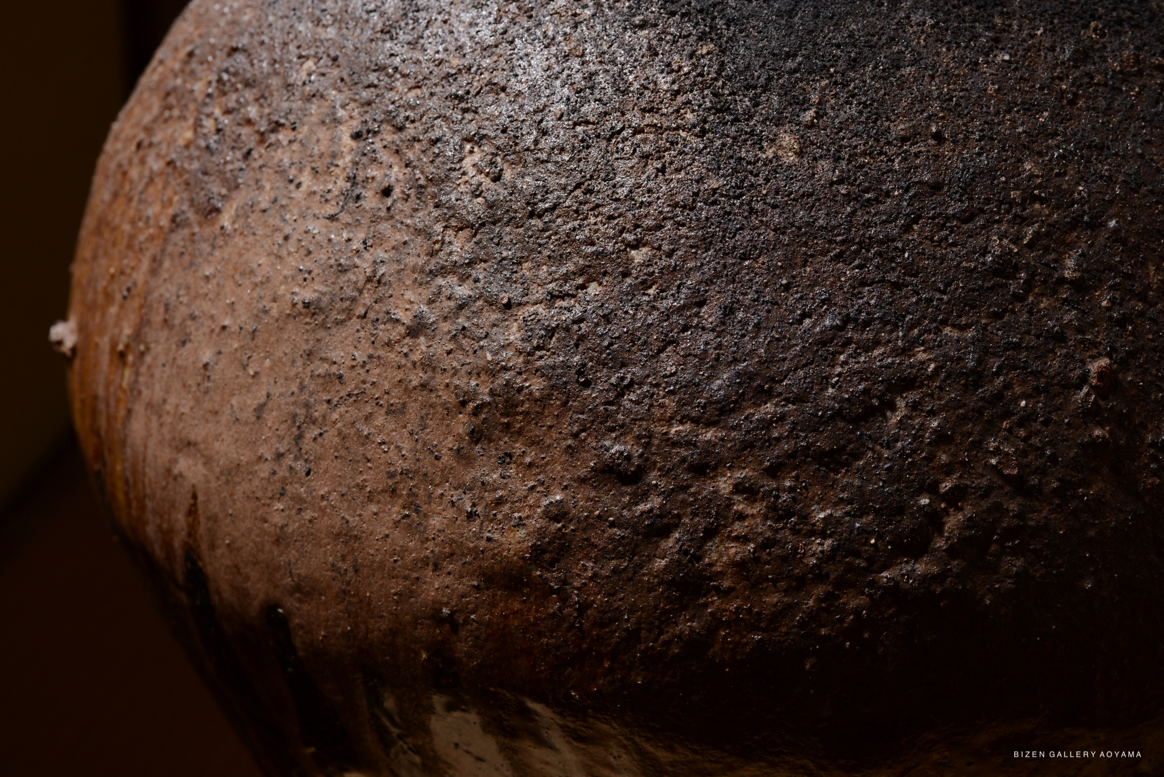 Close-up view of a Bizen Otsubo pottery piece, showcasing its textured surface with a mix of dark and earthy tones.