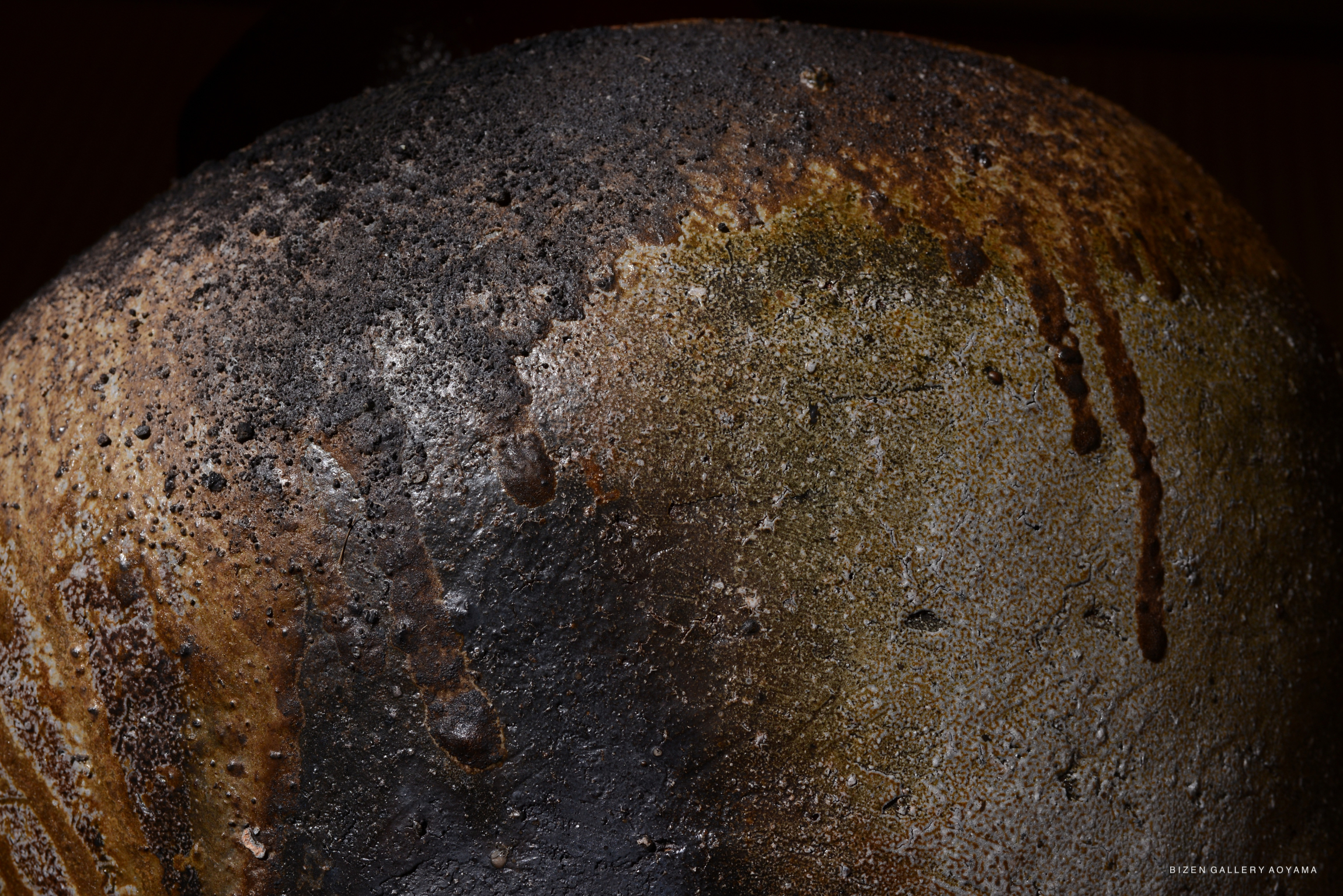 Close-up of a textured ceramic surface showcasing varying shades of brown, tan, and black, highlighting natural imperfections and drip patterns.