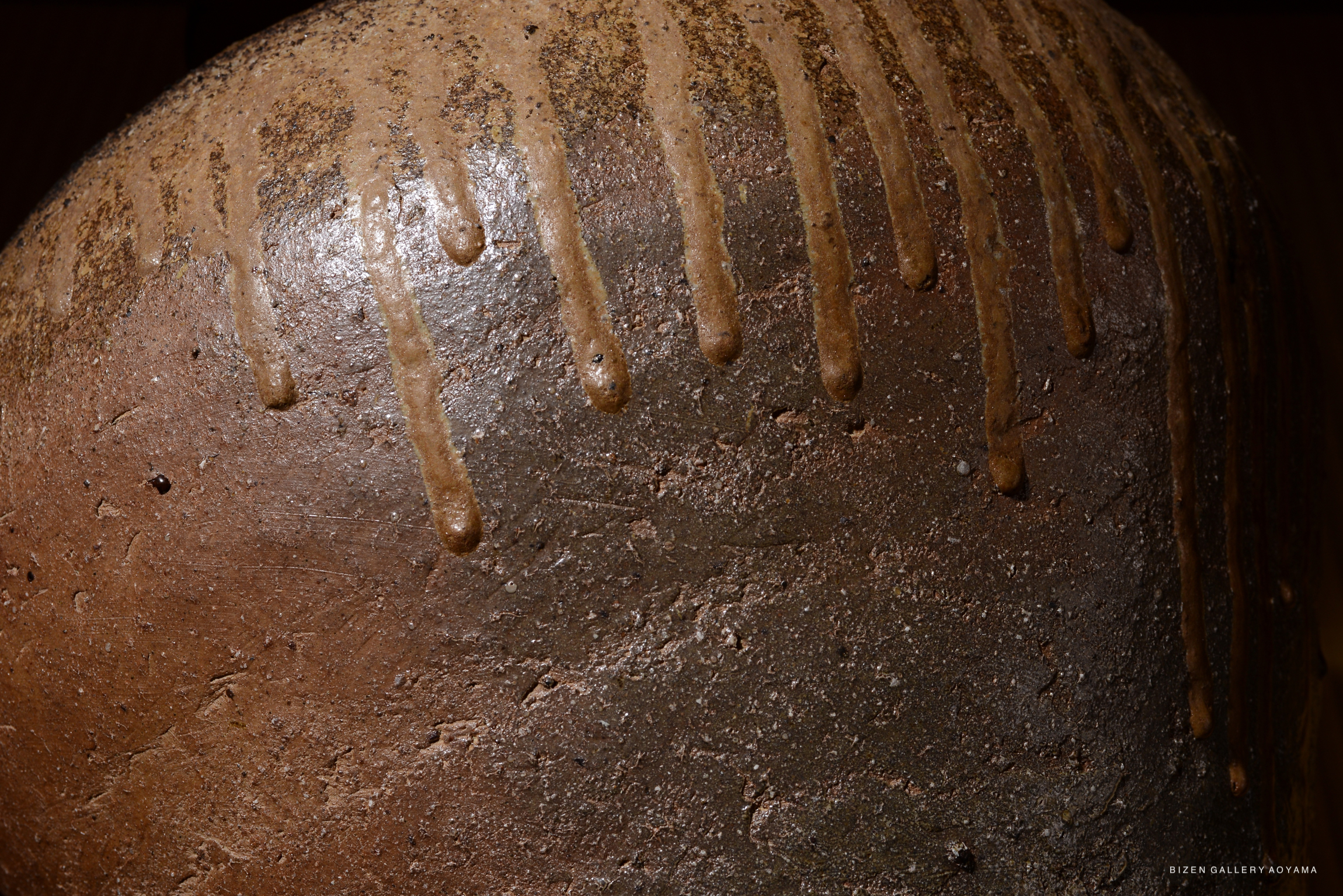 Close-up of a textured Bizen pottery piece, showcasing its earthy tones and distinctive drip patterns.