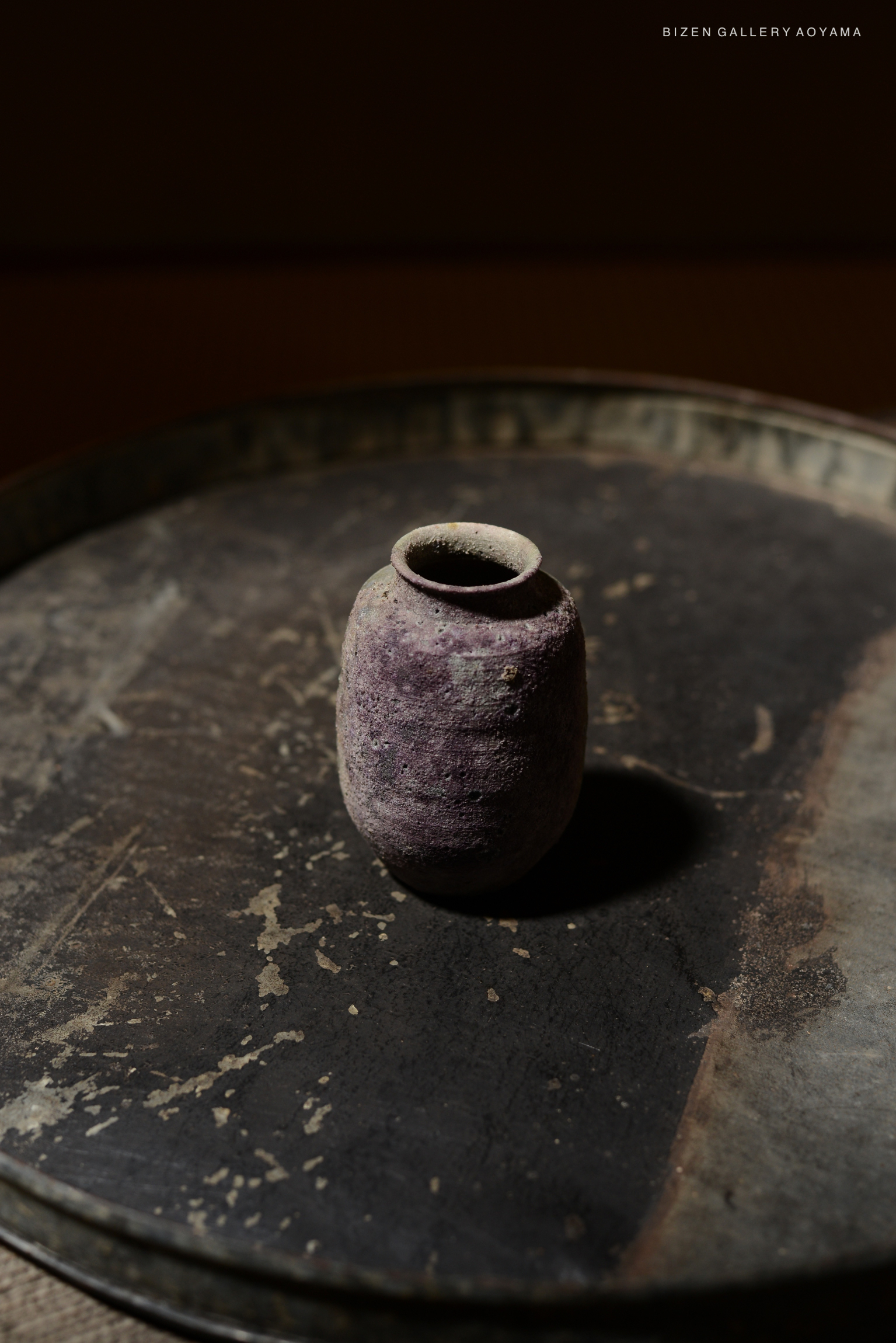 A small purple ceramic vase on a round, textured metallic surface.