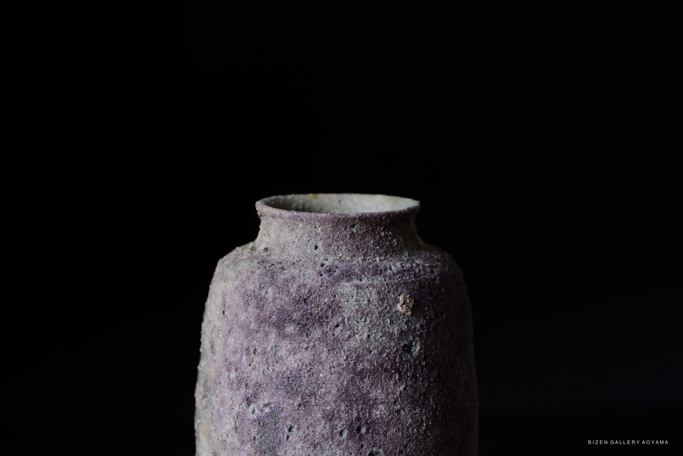 Close-up view of a textured purple ceramic vase on a black background.