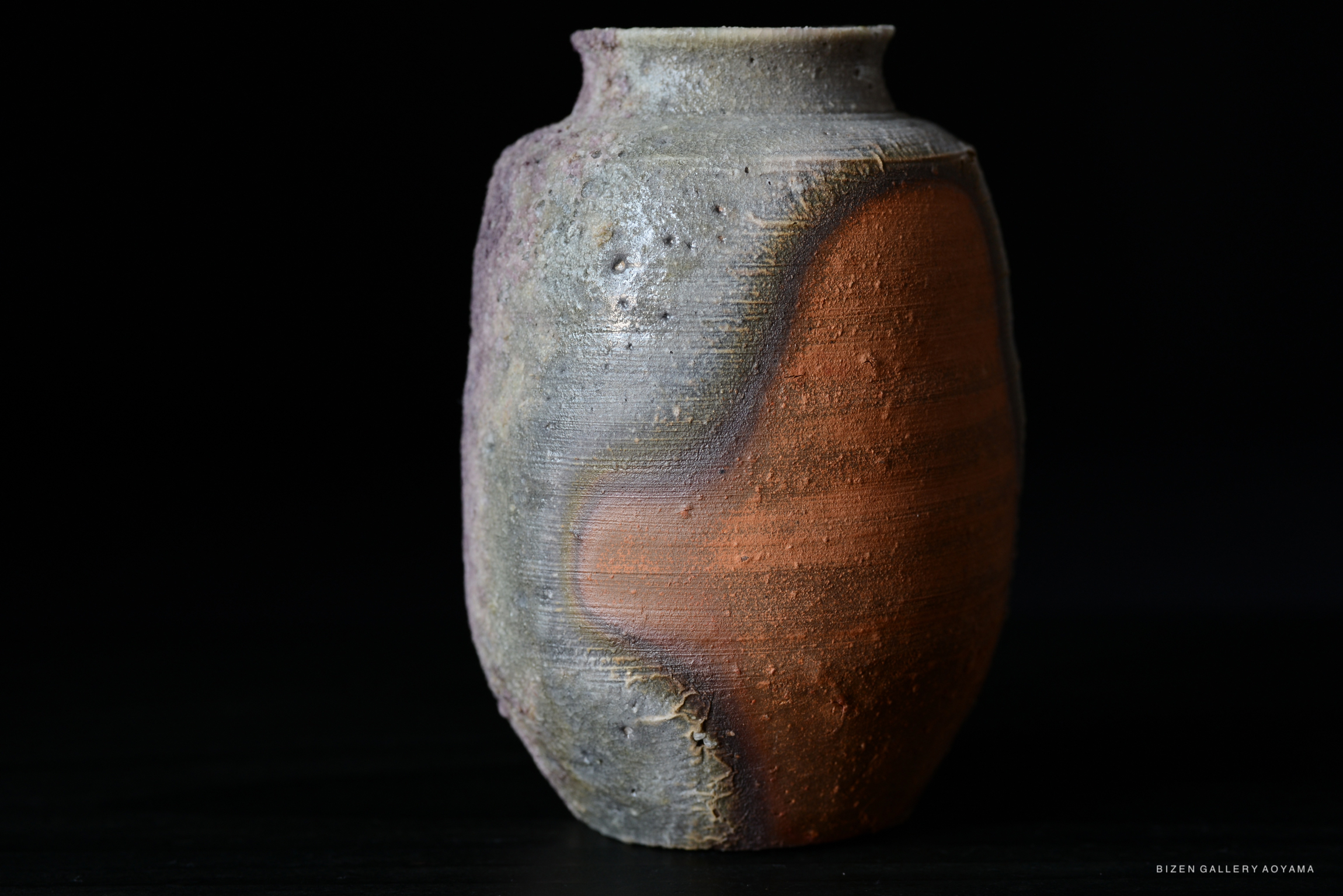 A unique Bizen pottery vase showcasing a blend of earthy tones and textures, set against a dark background.