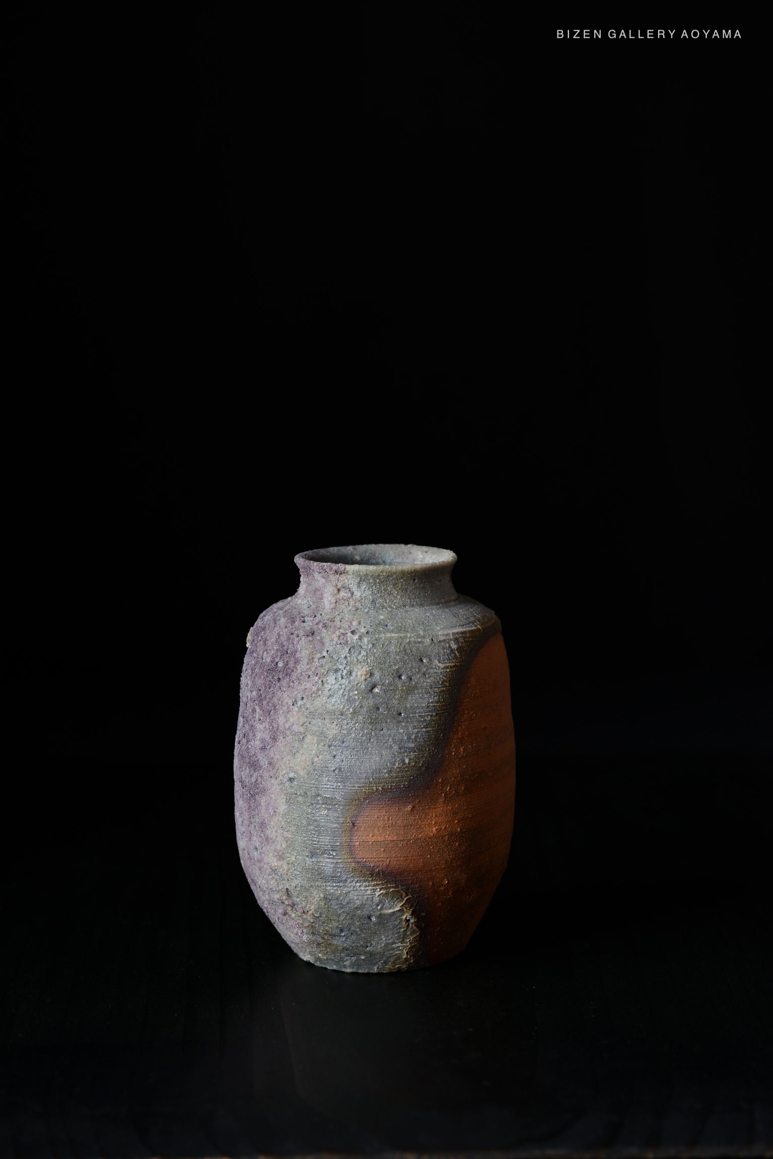 A ceramic vase with a textured surface and a two-tone design featuring earthy colors, displayed against a black background.