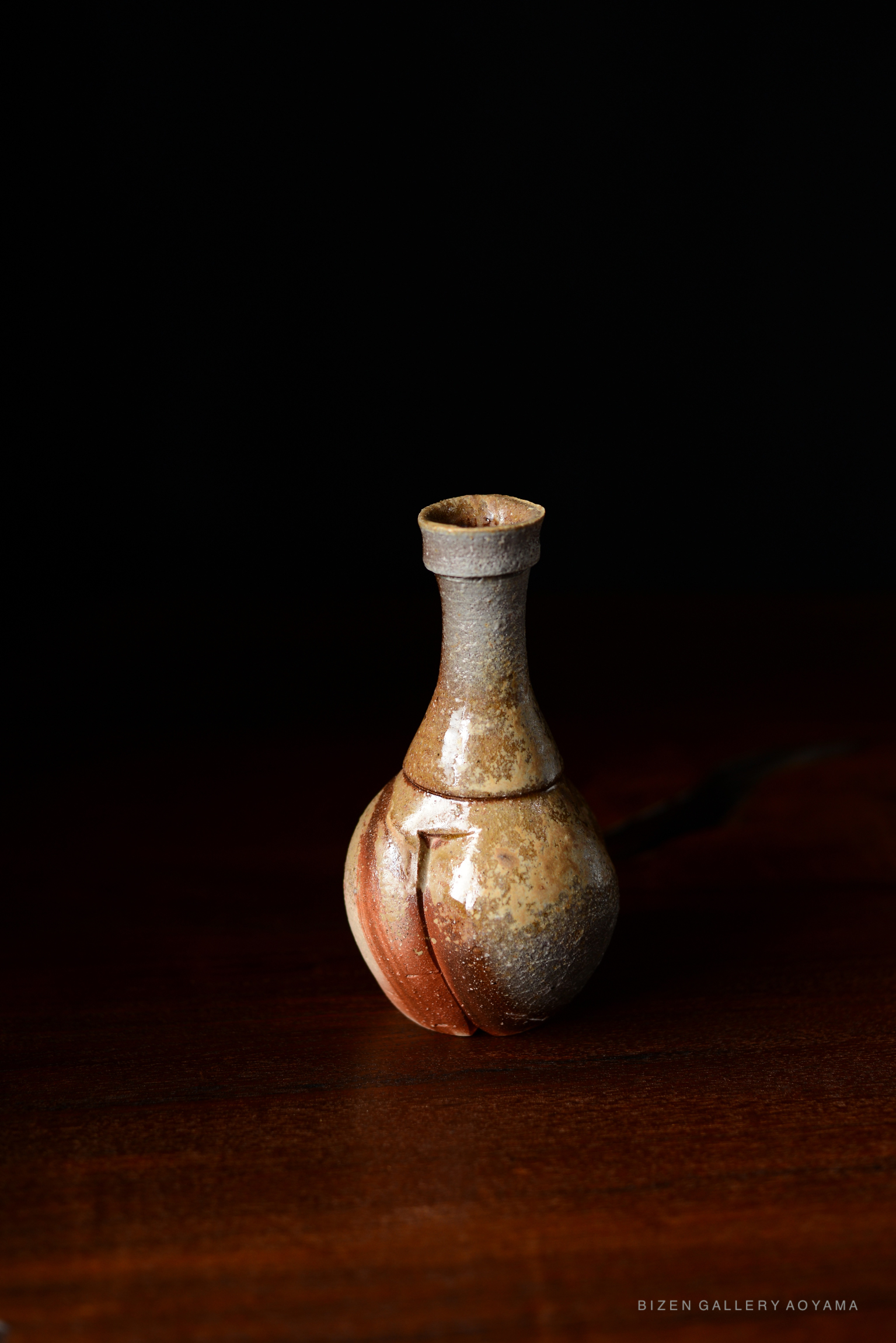 A Bizen tokkuri, a traditional Japanese sake bottle, with a unique shape and earthy glaze, set against a dark background.