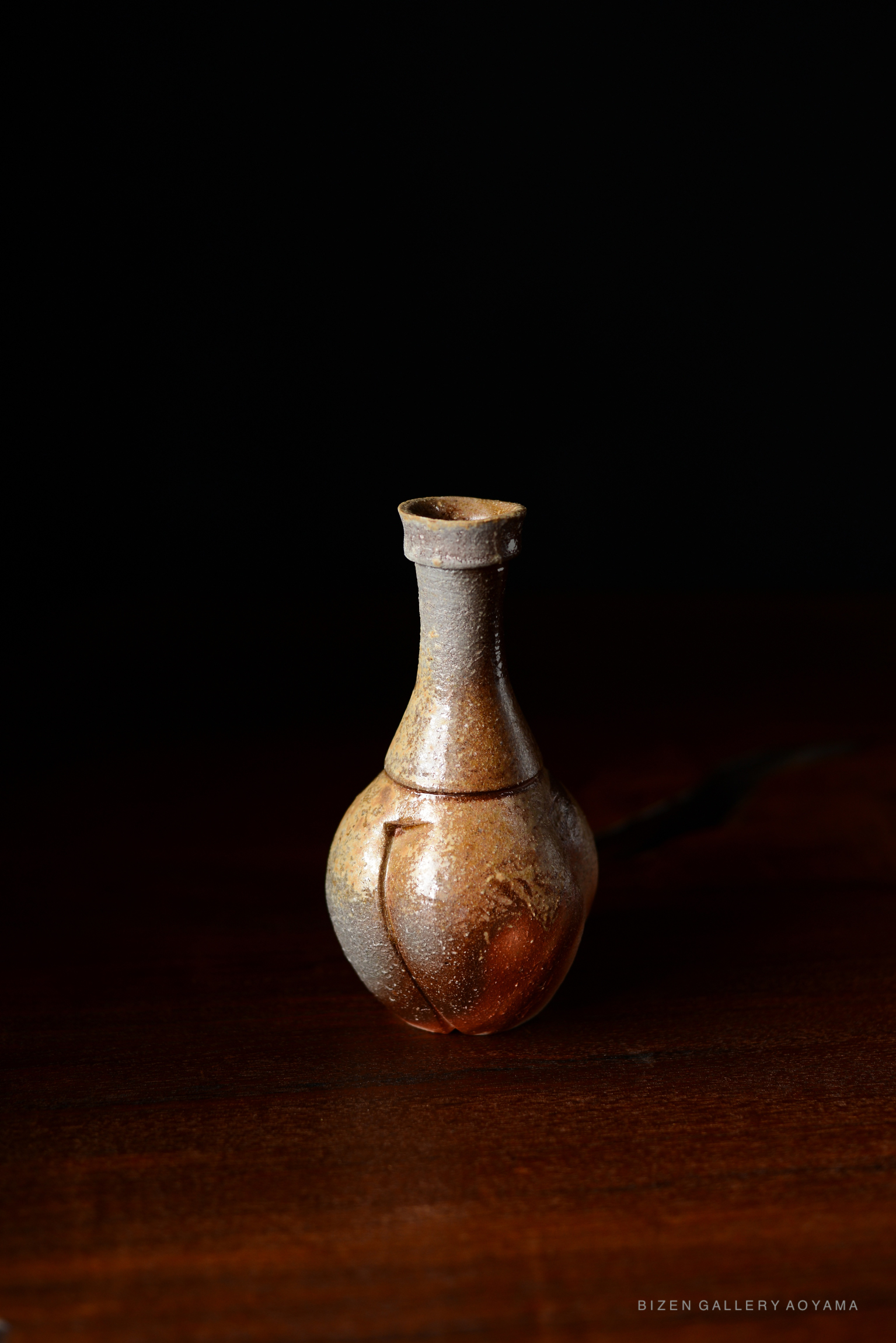 A Bizen Tokkuri, a traditional Japanese sake jug, featuring an elegant, rounded shape with a textured surface and subtle earthy colors, displayed against a dark background.