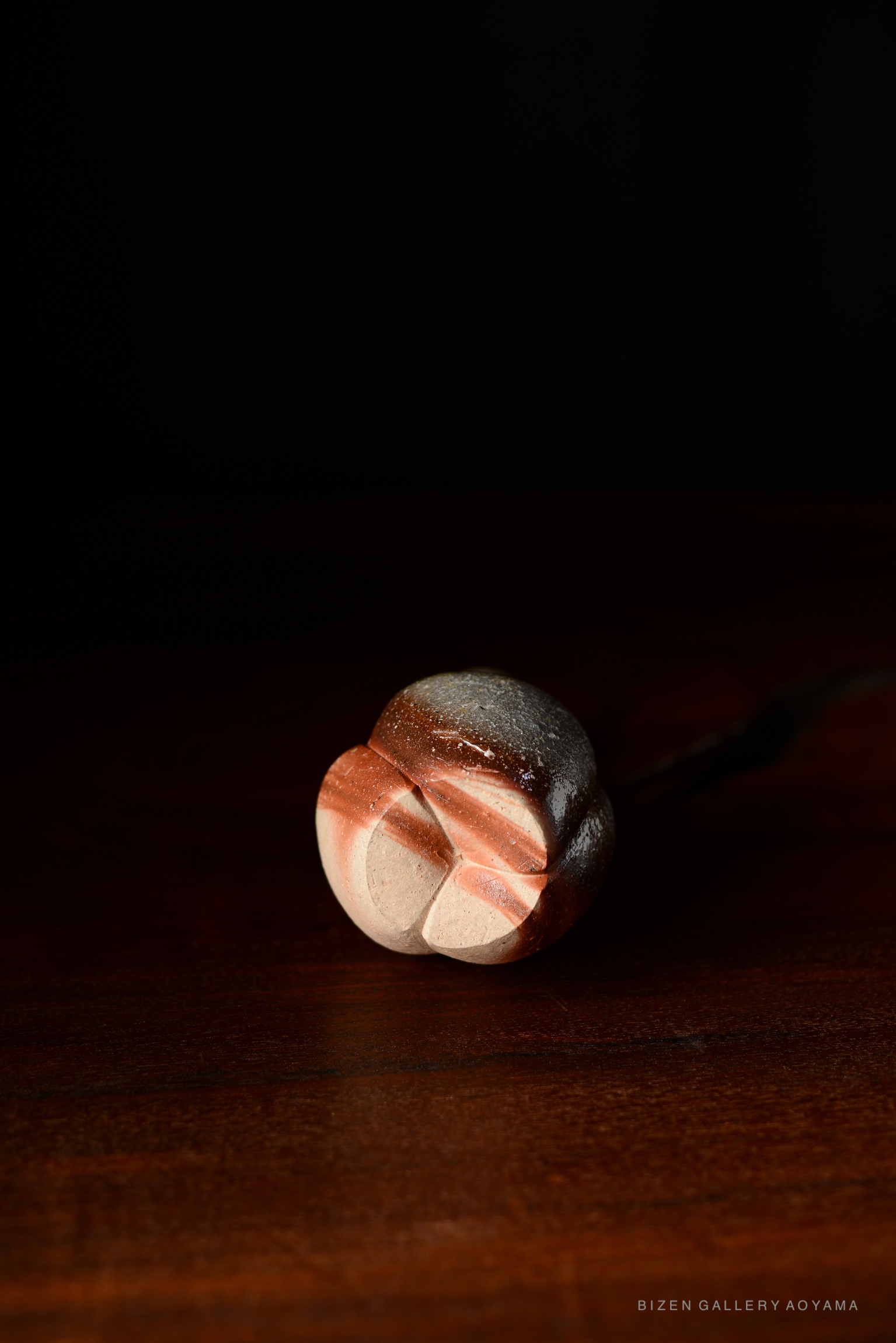 A Bizen pottery tokkuri with a distinctive shape and natural clay patterns, resting on a wooden surface against a dark background.