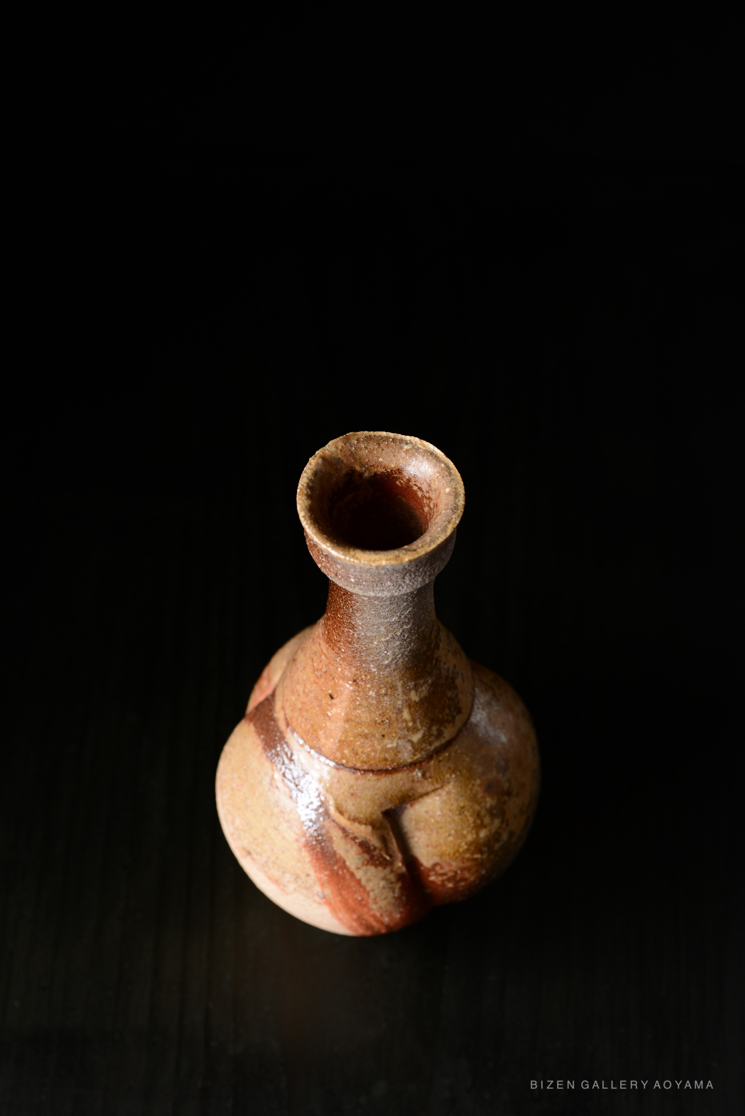 A top-down view of a Bizen Tokkuri, a traditional Japanese ceramic sake bottle, showcasing its unique shape and earthy color against a dark background.
