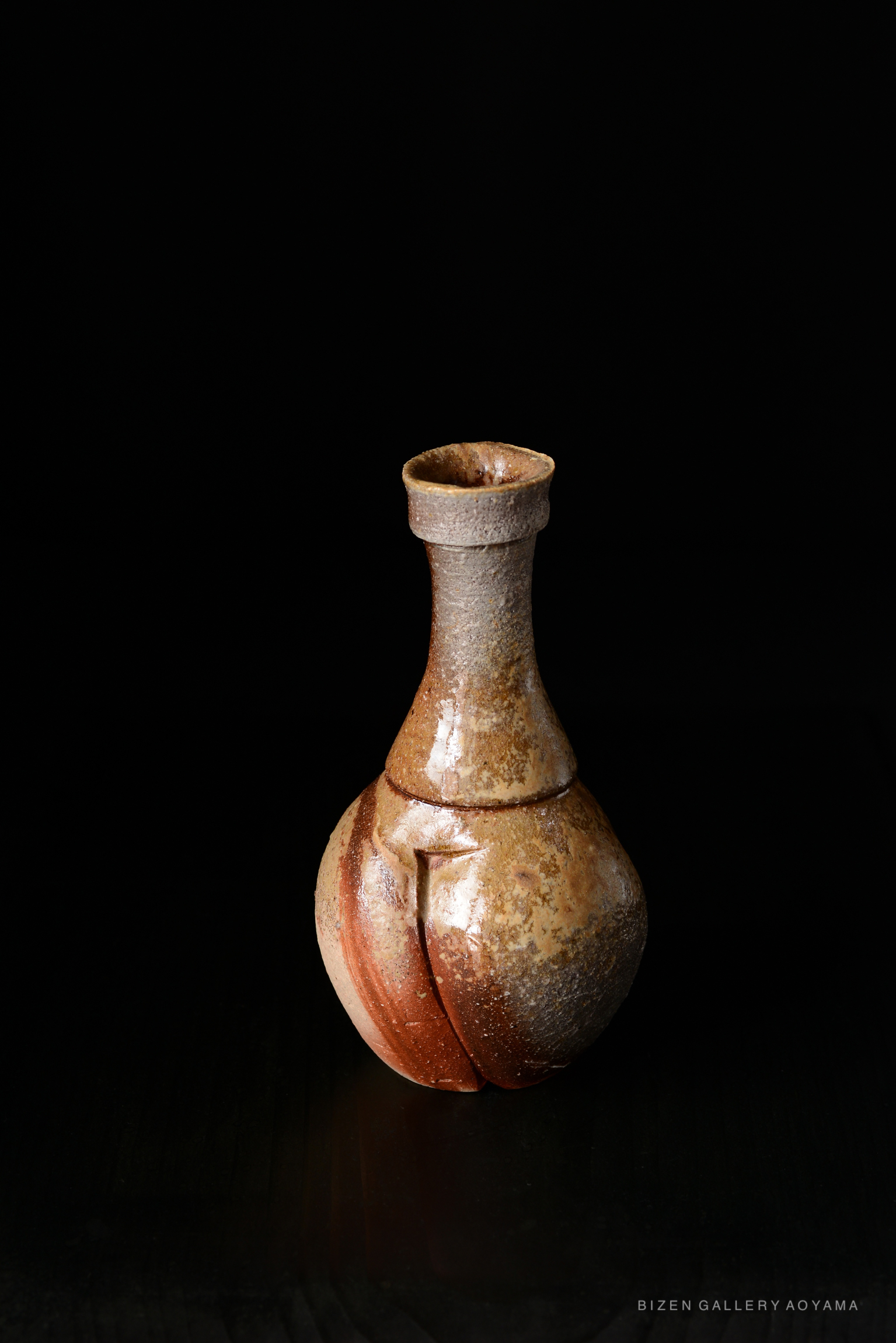 A Bizen tokkuri, a traditional Japanese sake vessel, featuring a distinctive rounded body and a narrow neck, displayed against a black background.