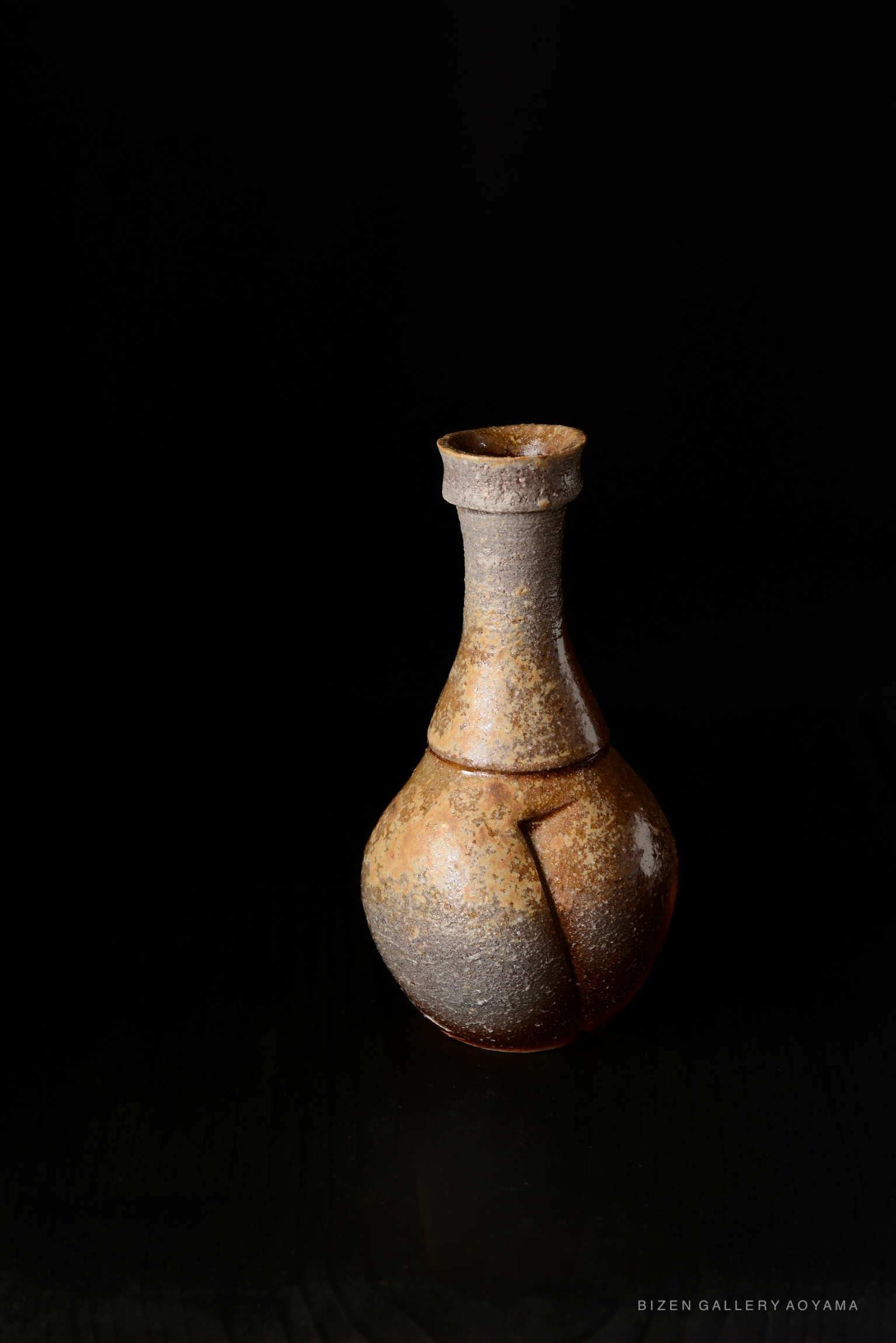 A Bizen tokkuri, a traditional Japanese ceramic sake bottle, featuring a unique, rustic glaze with earthy tones and a distinctive shape, set against a dark background.